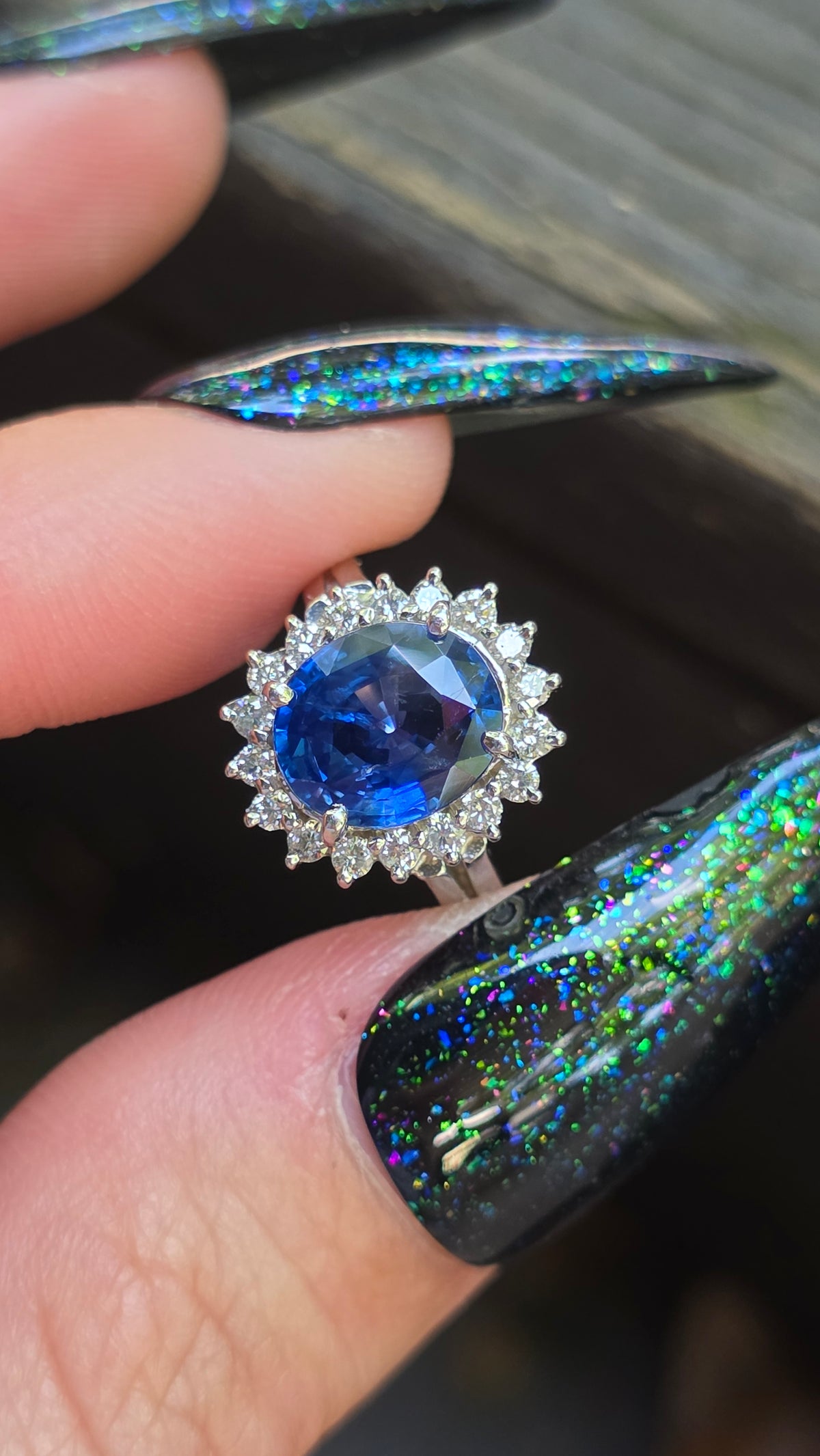 Close-up of a blue gemstone ring held between fingers with colorful nail polish.