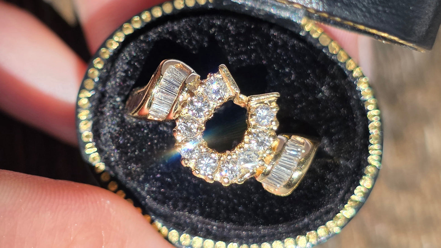 A gold ring with a central marquise-cut gemstone and baguette side stones, displayed inside an open black velvet ring box held by a hand.