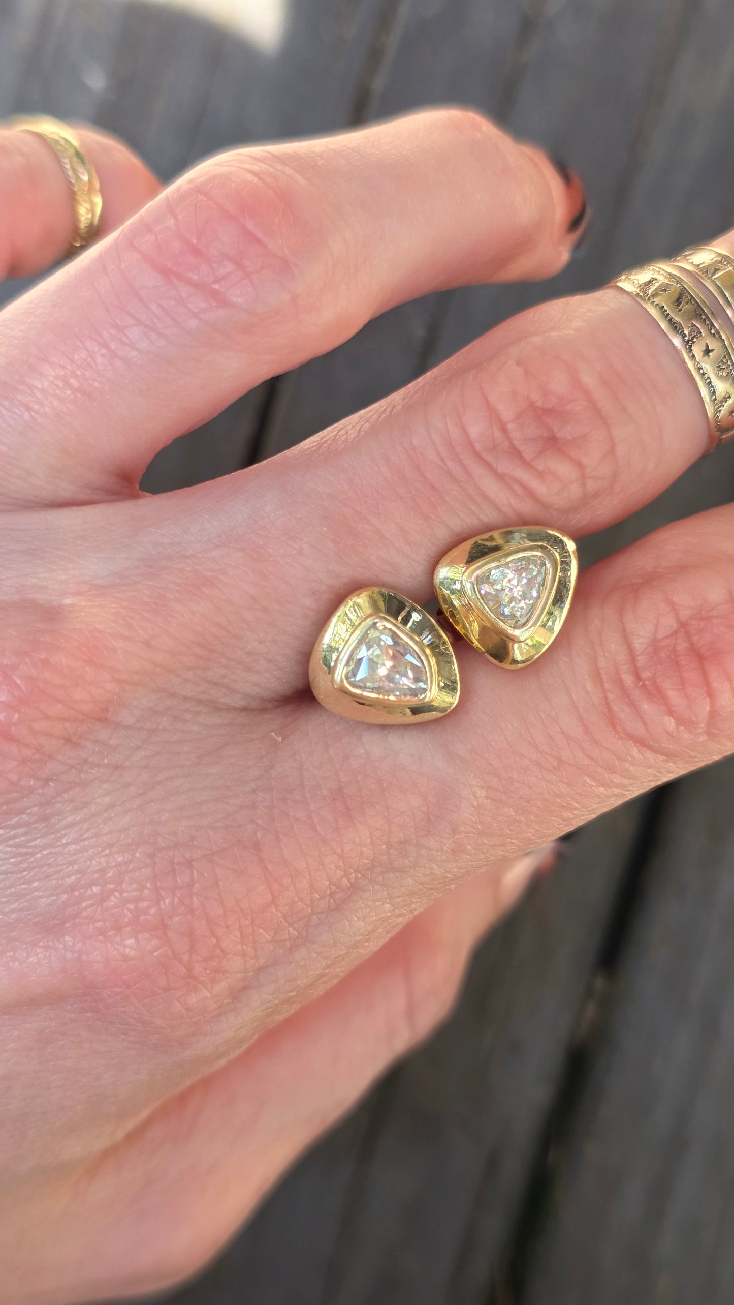 A close-up of a hand wearing two gold heart-shaped rings with clear gemstones in the center, set against a dark wooden background.