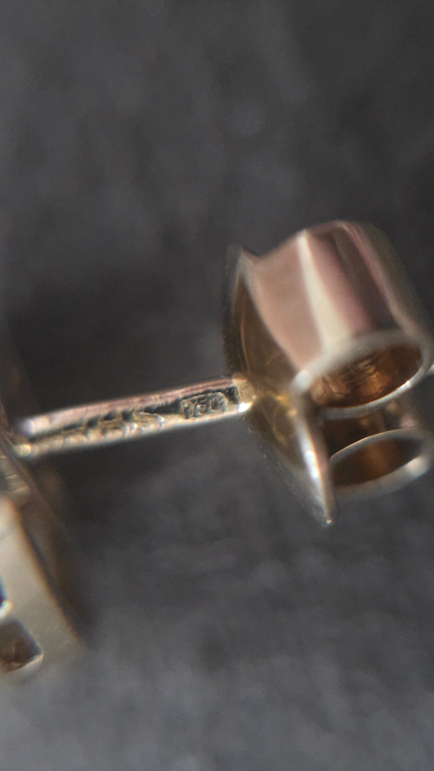 A close-up of a silver-toned stud earring with a faceted, geometric post and a flat rectangular backing, shown on a dark textured background.