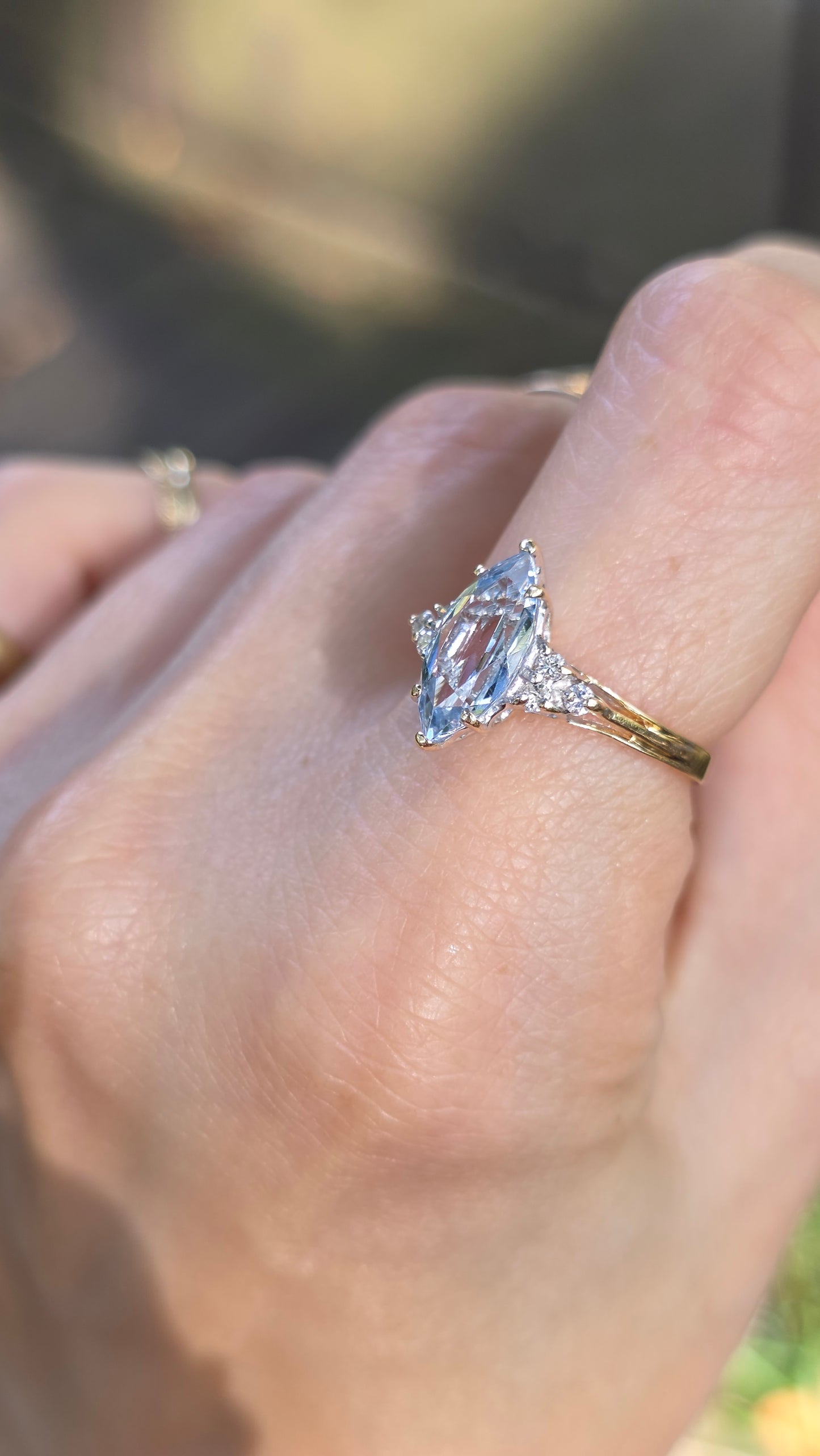 A close-up of a hand wearing a ring with a marquise-cut clear gemstone in a silver-toned setting on a gold band.