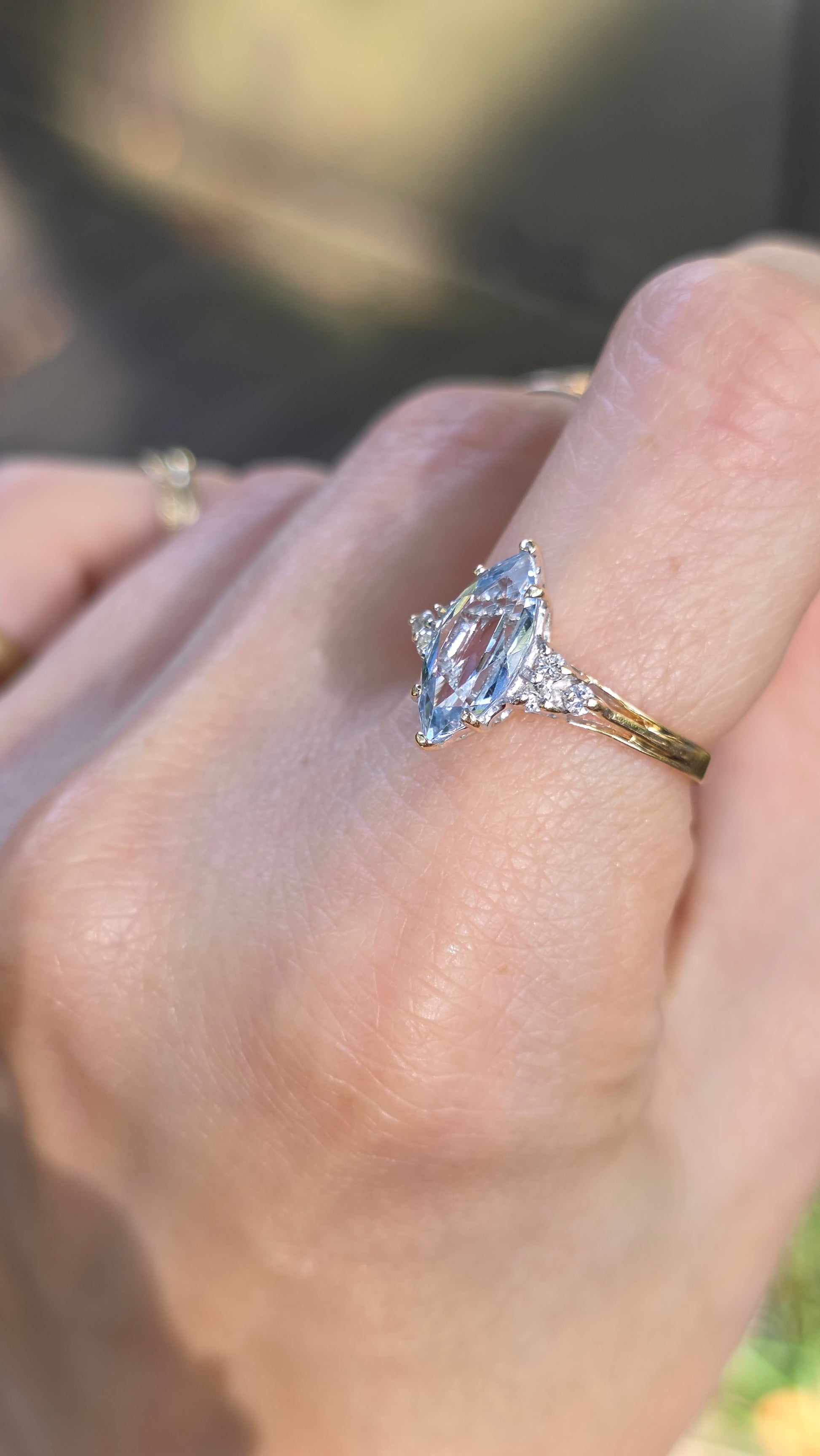 A close-up of a hand wearing a ring with a marquise-cut clear gemstone in a silver-toned setting on a gold band.