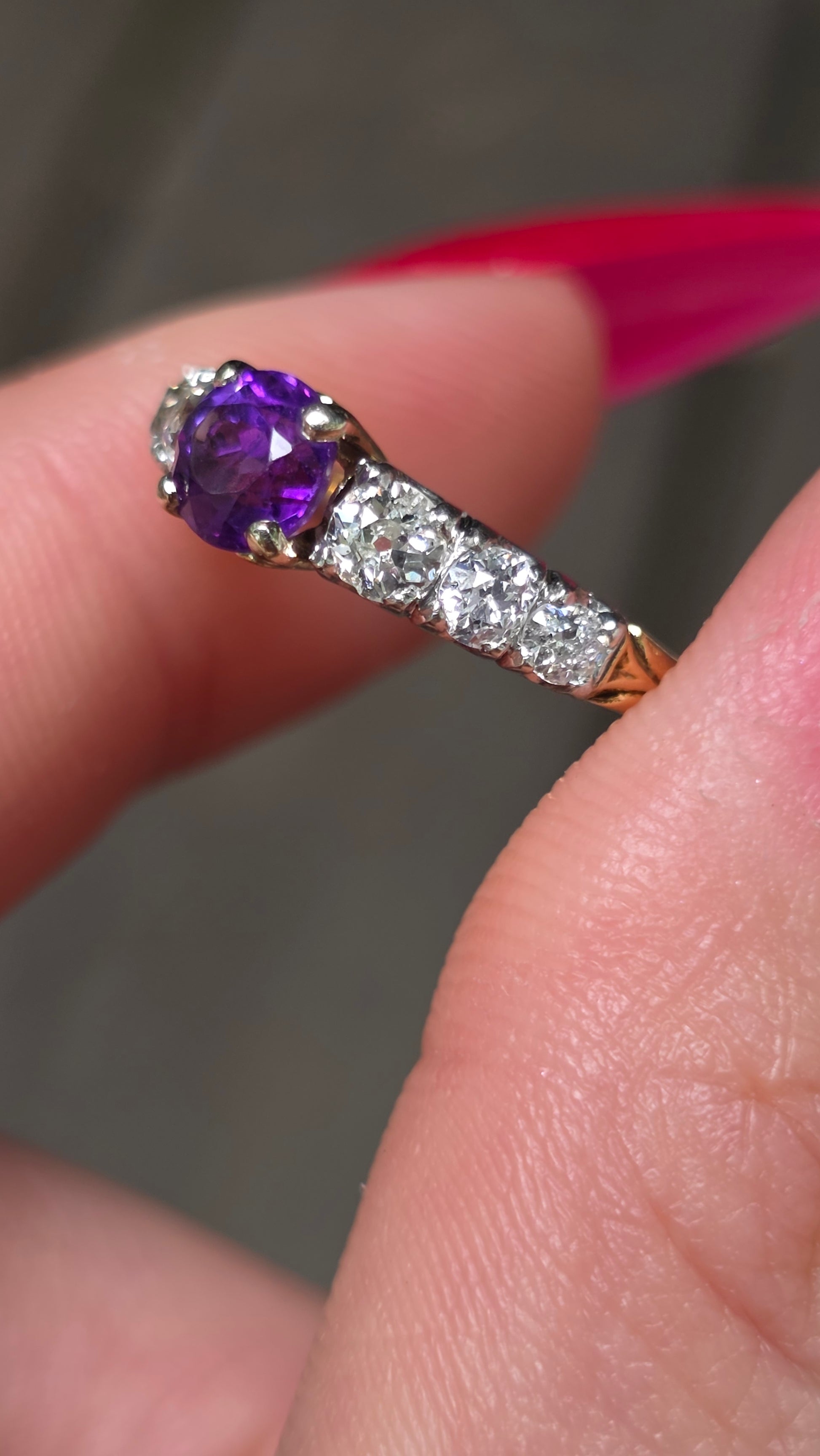 Close-up of a hand wearing a ring with a purple gemstone and diamond accents.