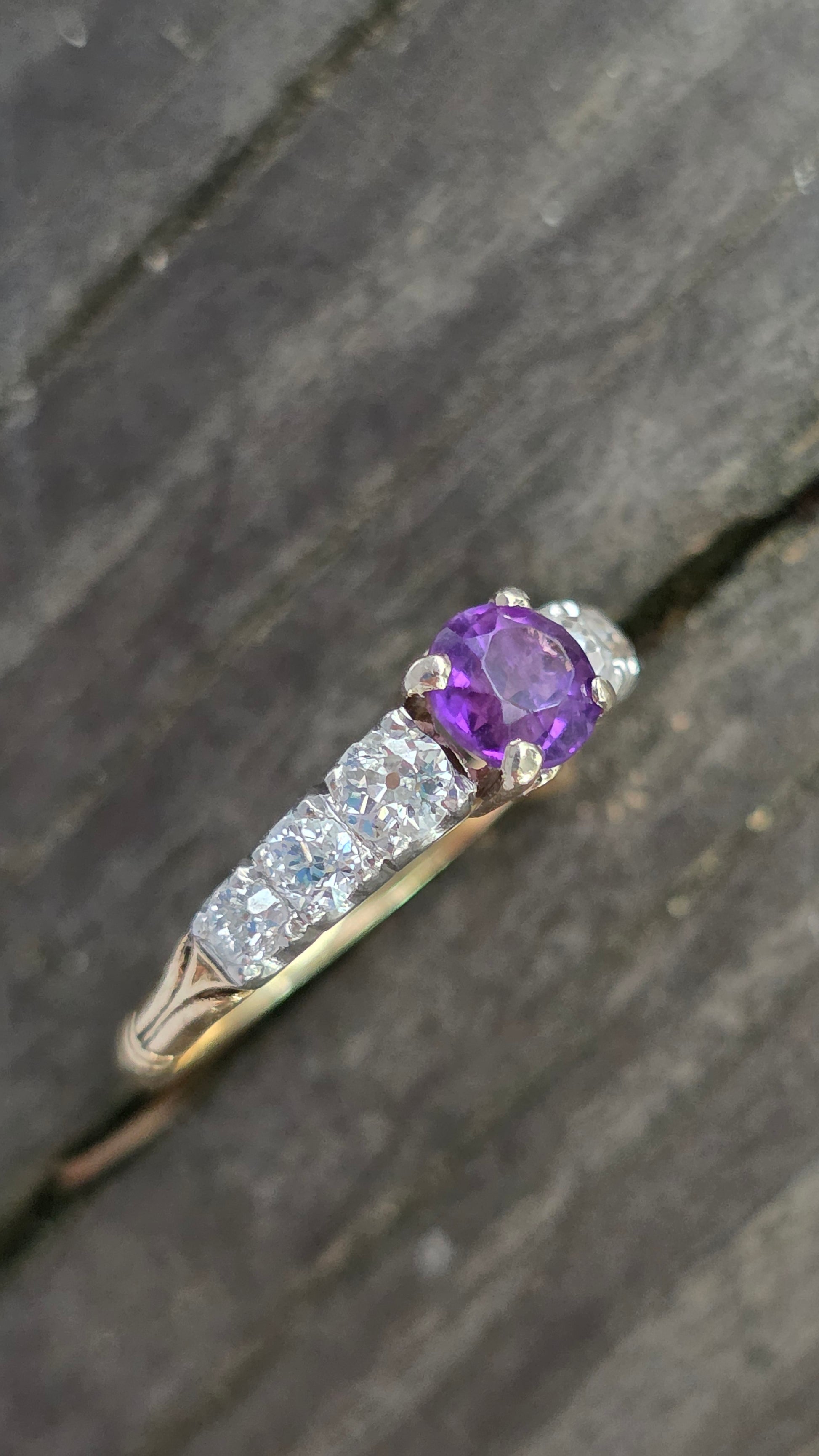 Ring with purple gemstone and diamond accents on a dark wooden surface