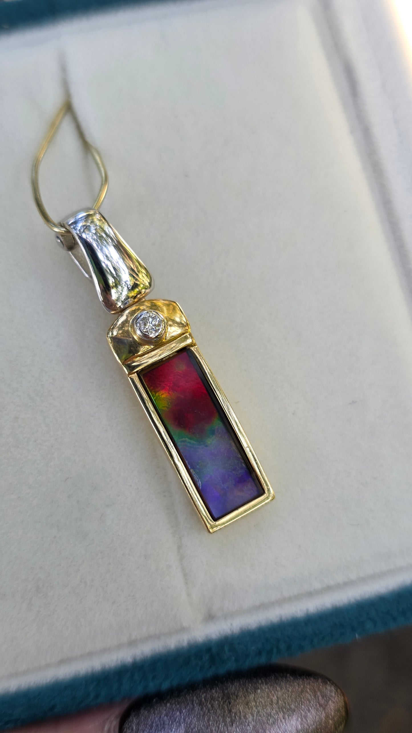 Gold pendant with a colorful stone and diamond on a light background