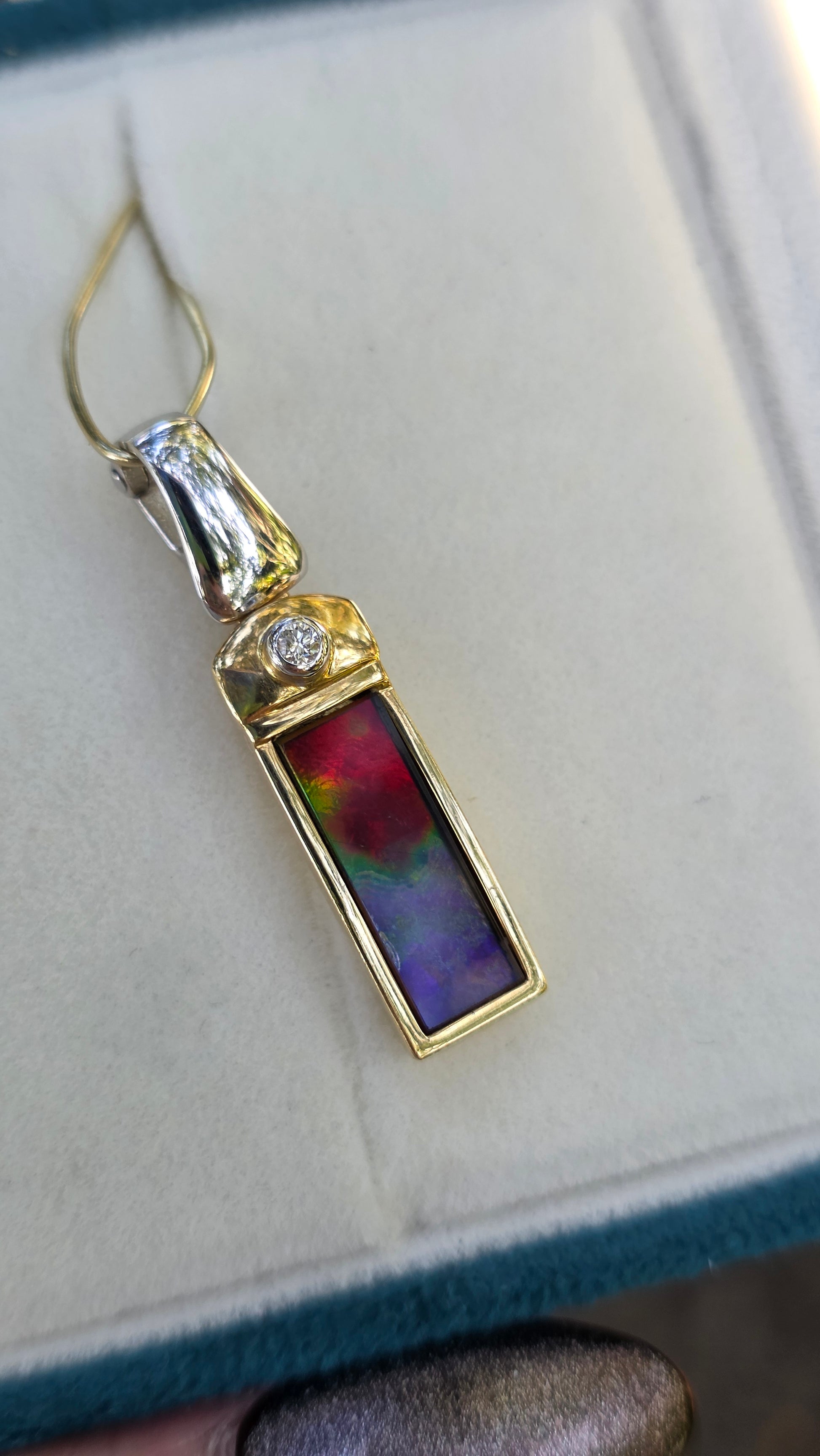 Gold pendant with a colorful stone and diamond on a light background