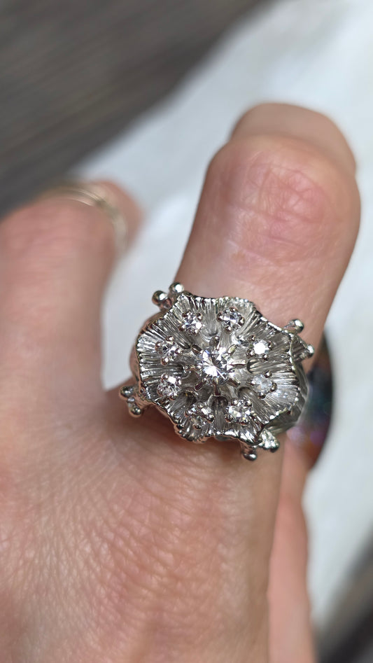A close-up of a silver-toned cluster ring with multiple clear gemstones worn on a finger.