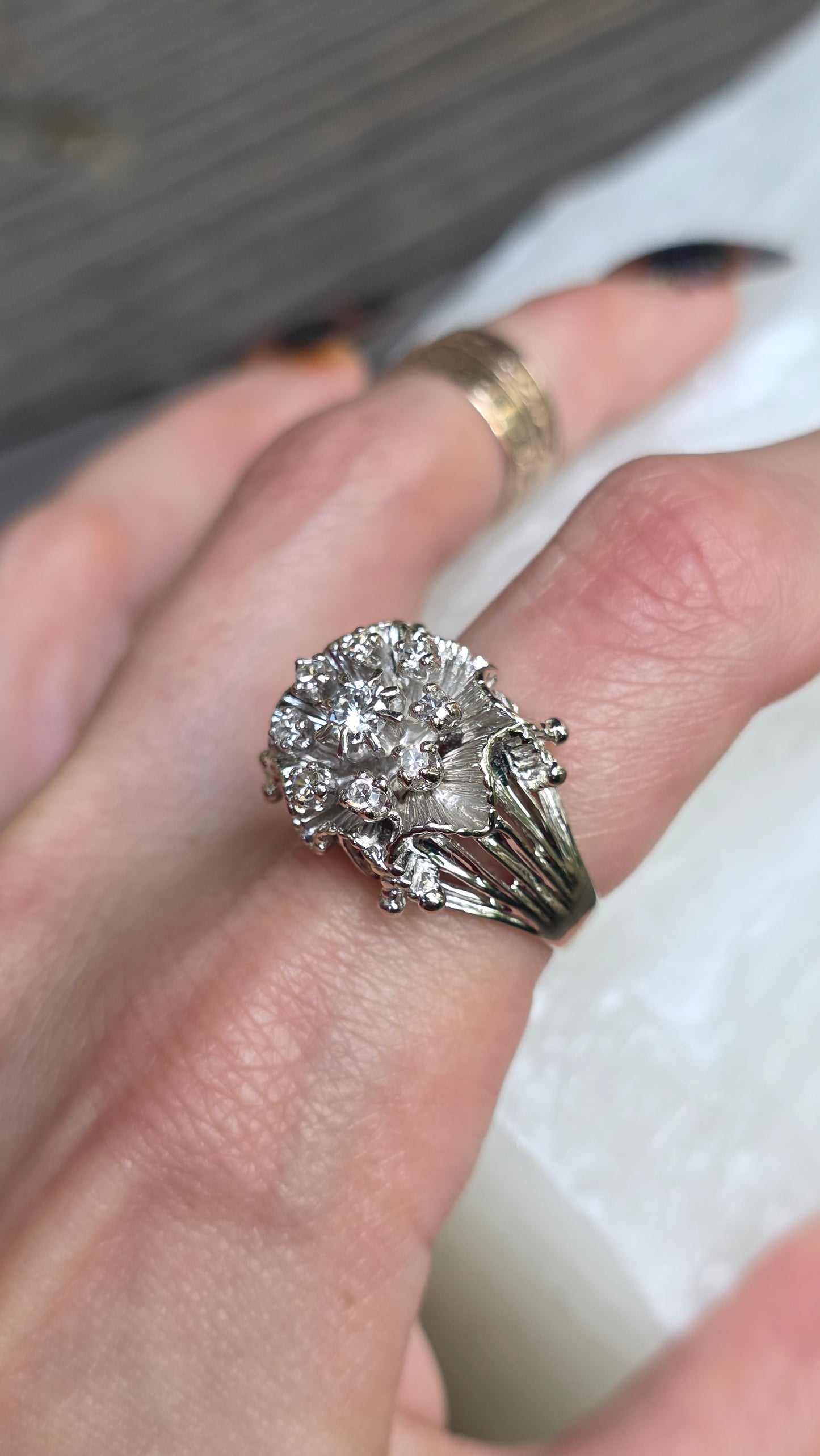 A close-up of a hand wearing a silver-toned cluster ring with multiple clear stones, alongside another gold-toned ring on the same finger.