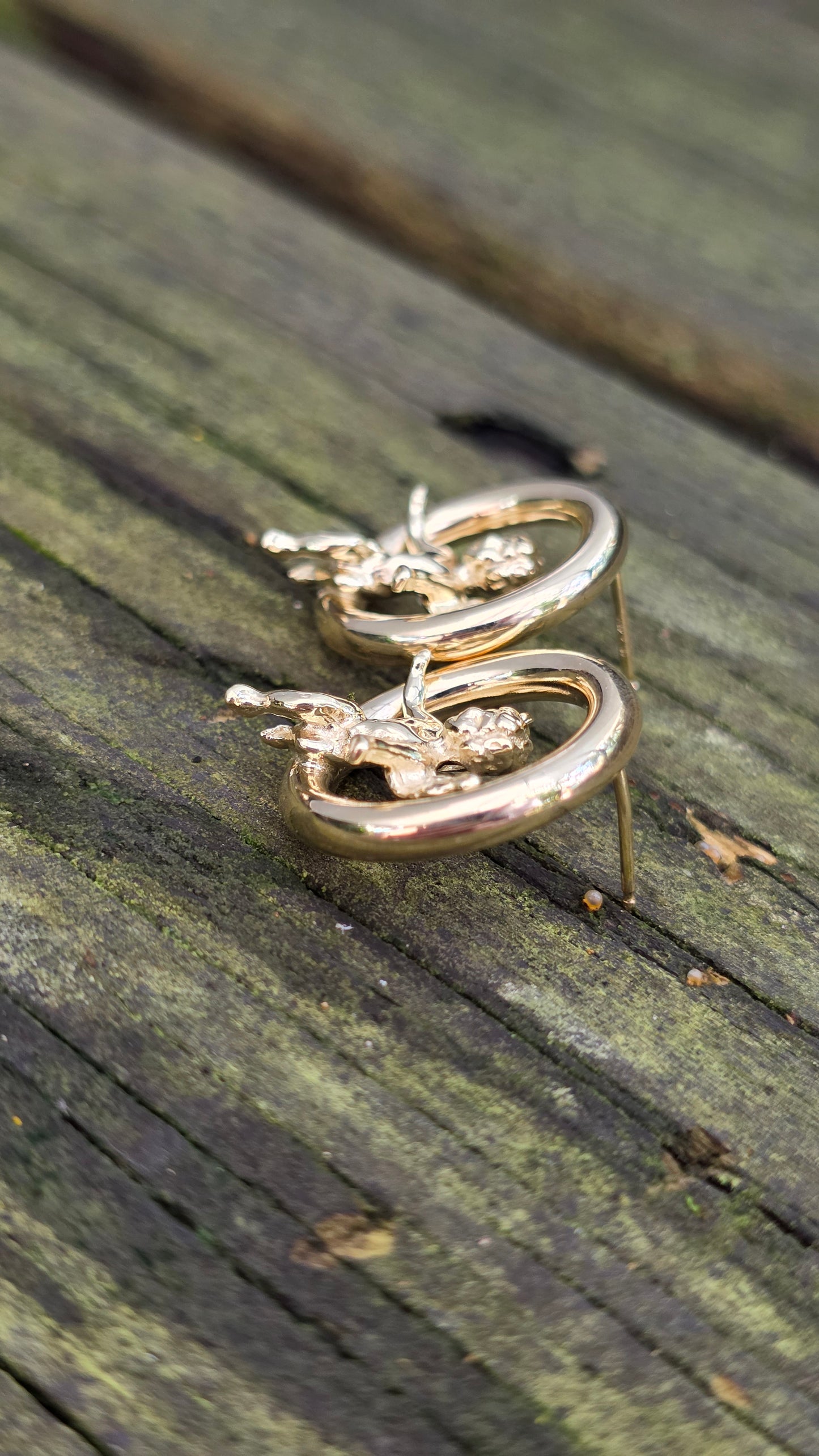 Gold earrings with angel designs on a wooden surface