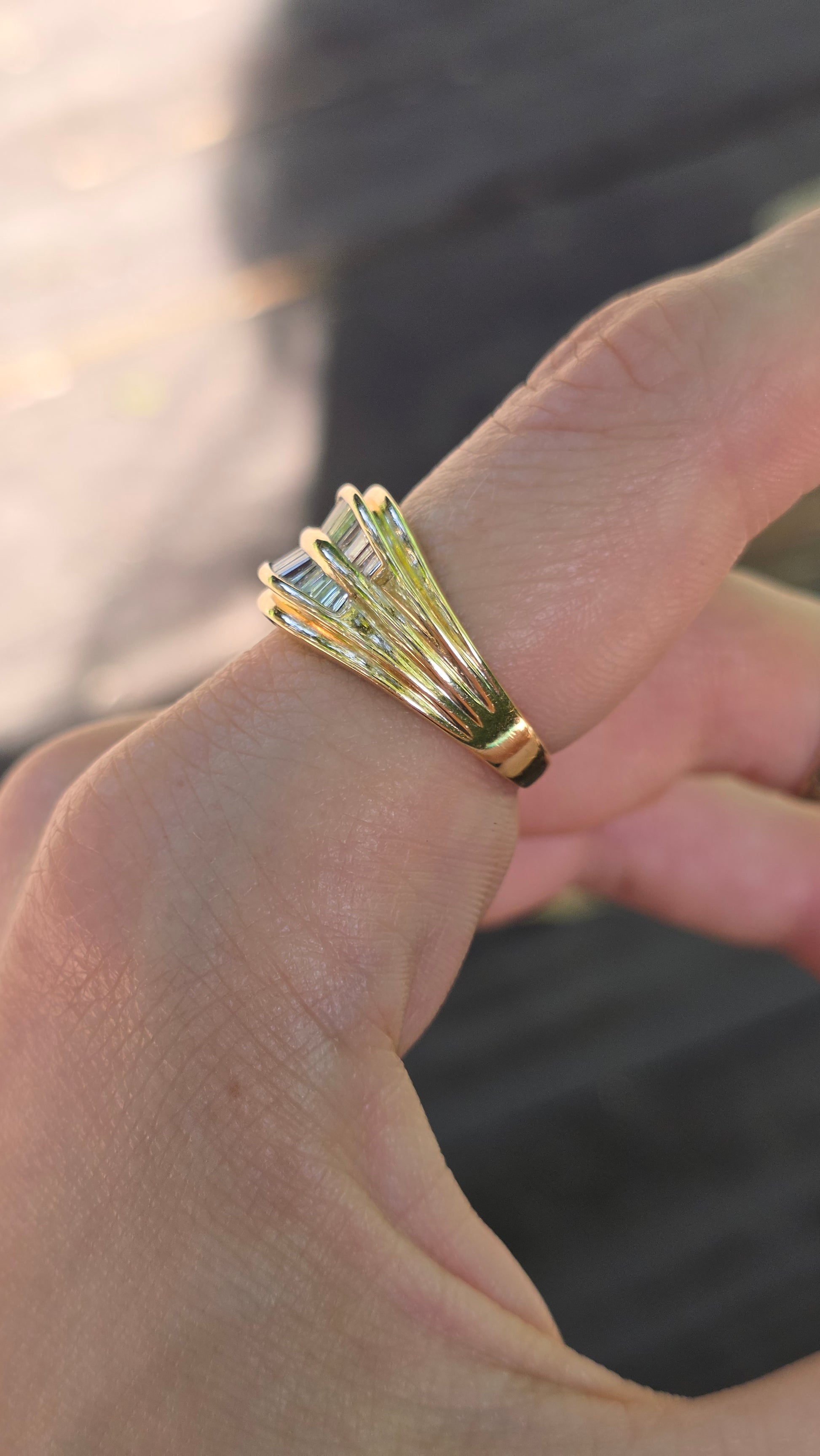 A gold ring with a textured, layered fan-like design worn on a person's finger, shown in a close-up shot.
