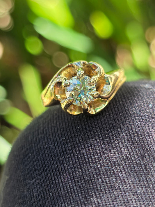 Gold ring with a diamond on a black cushion against a blurred green background