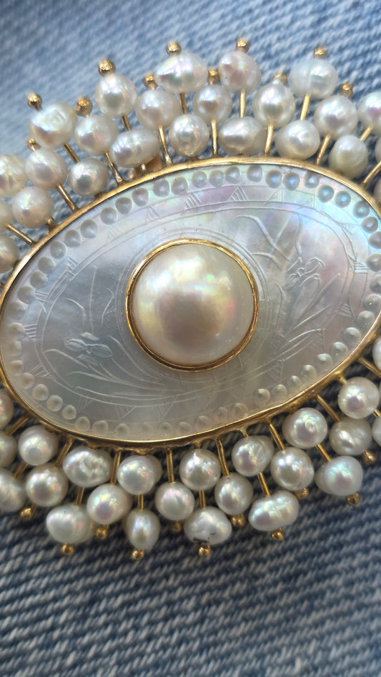 Pearl-encrusted brooch with a central pearl on a textured fabric background