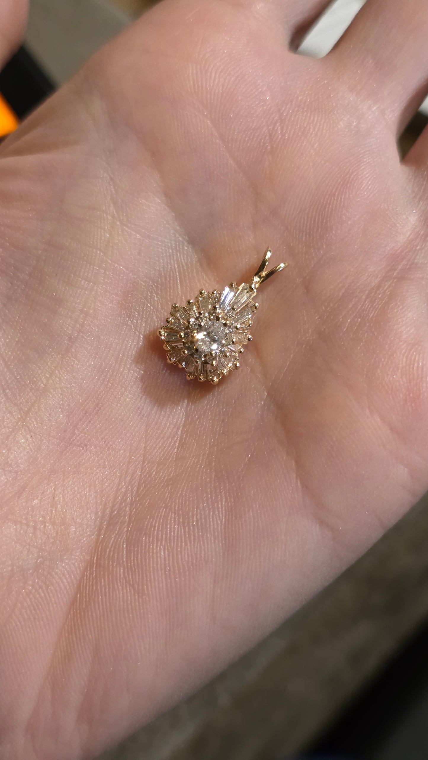 A small gold pendant with a cluster of clear stones, resting on an open palm.