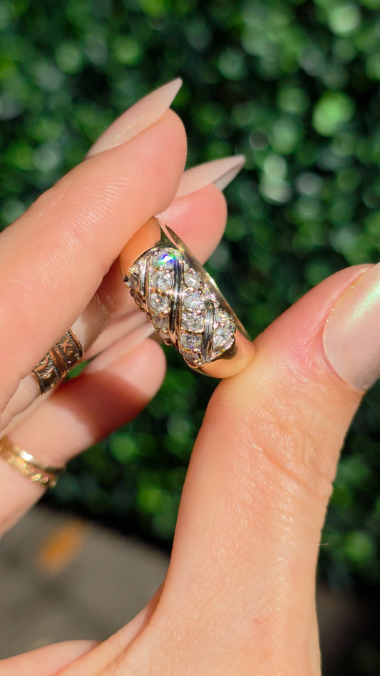 A close-up of a hand holding a gold ring with multiple clear pavé-set stones against a blurred green outdoor background.