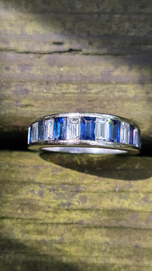 White gold ring with diamonds and blue gemstones on a wooden surface