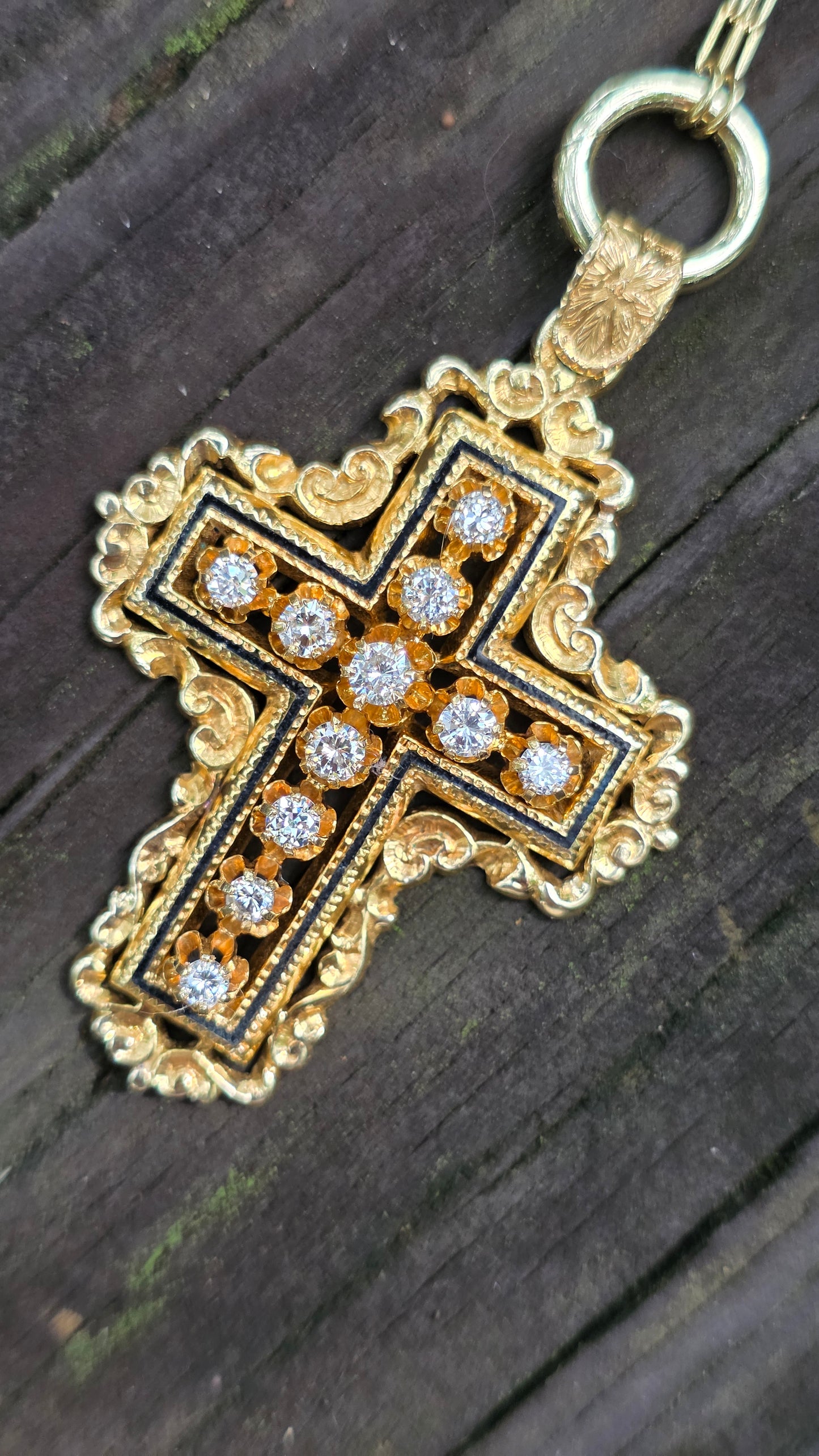 Gold and black cross pendant with embedded diamonds on a dark wooden surface