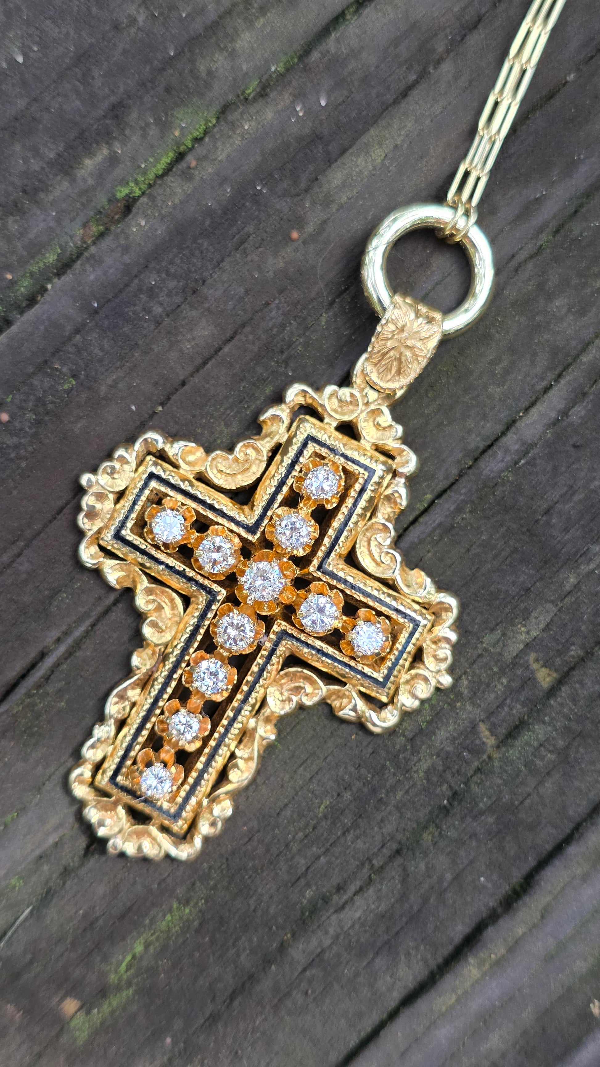 Gold cross pendant with embedded stones on a dark wooden surface