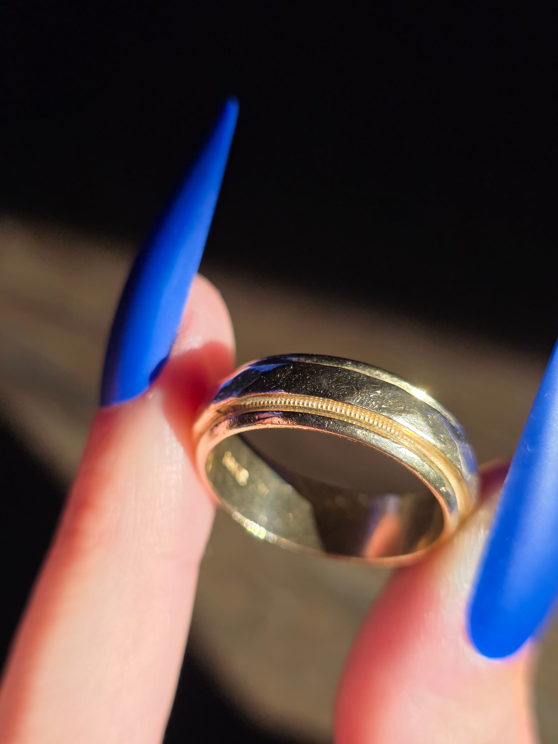 Gold ring held between blue finger nails with a blurred background