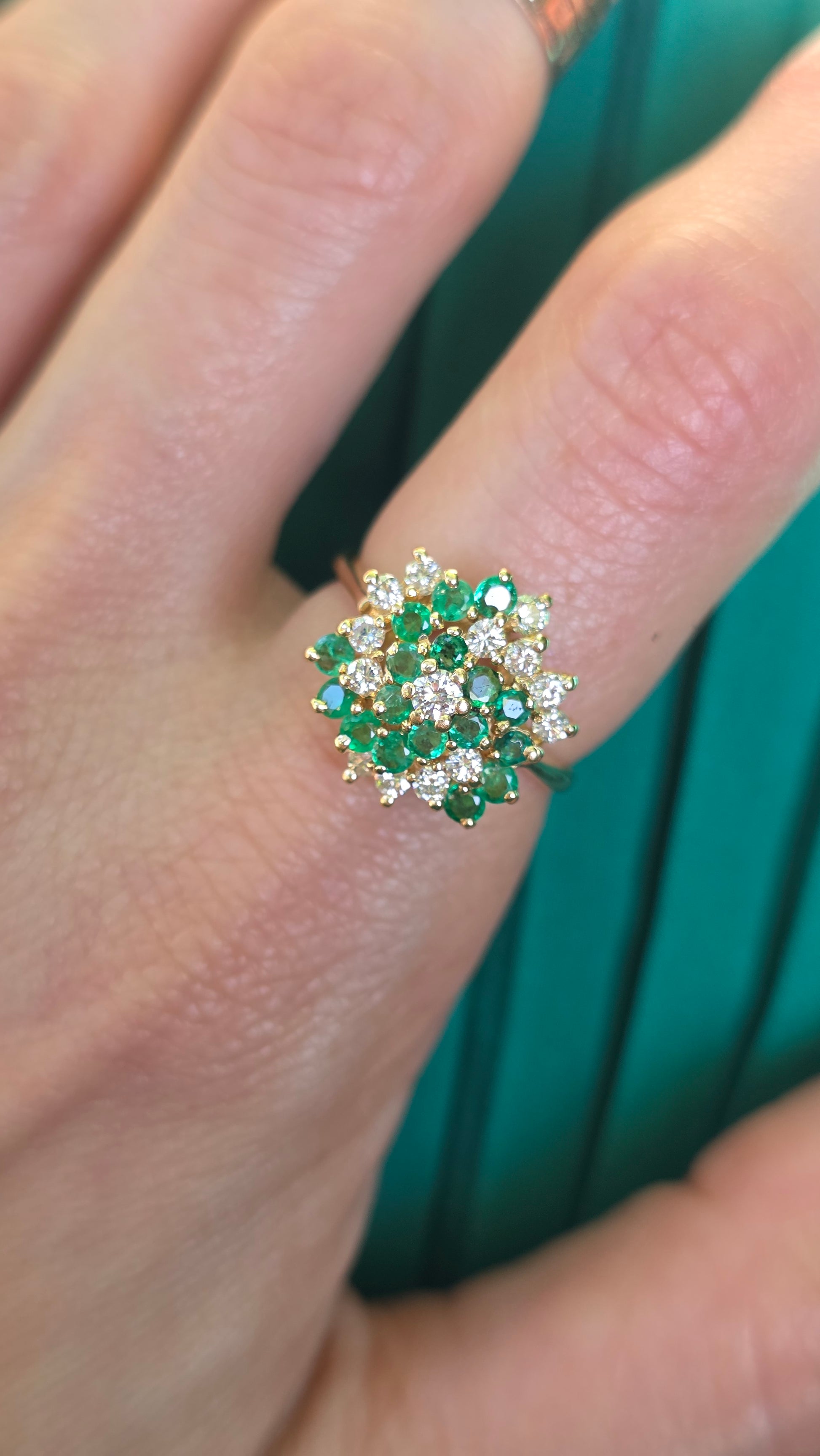 A close-up of a hand wearing a gold ring with a floral cluster of green and clear stones.