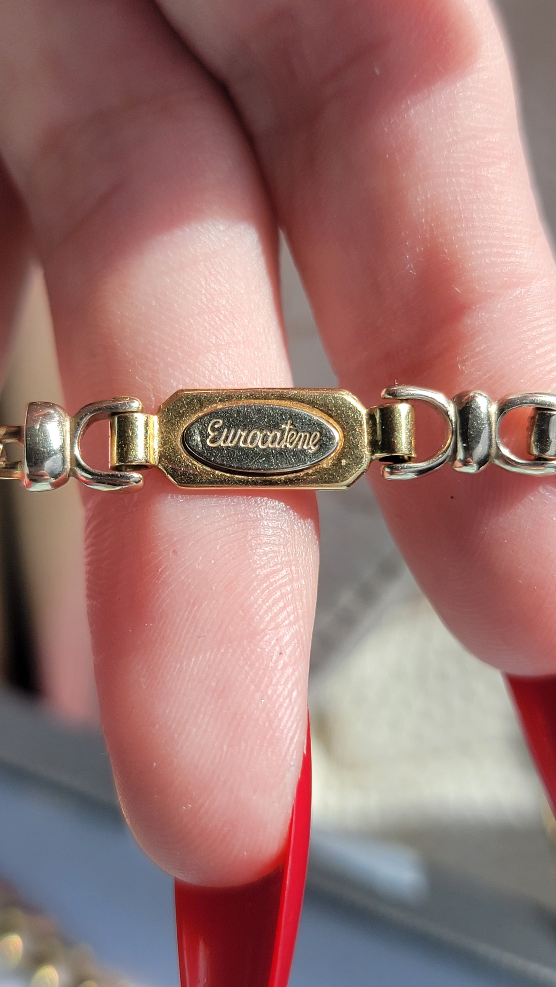 Close-up of a gold and silver bracelet with a visible brand logo on a blurred background.