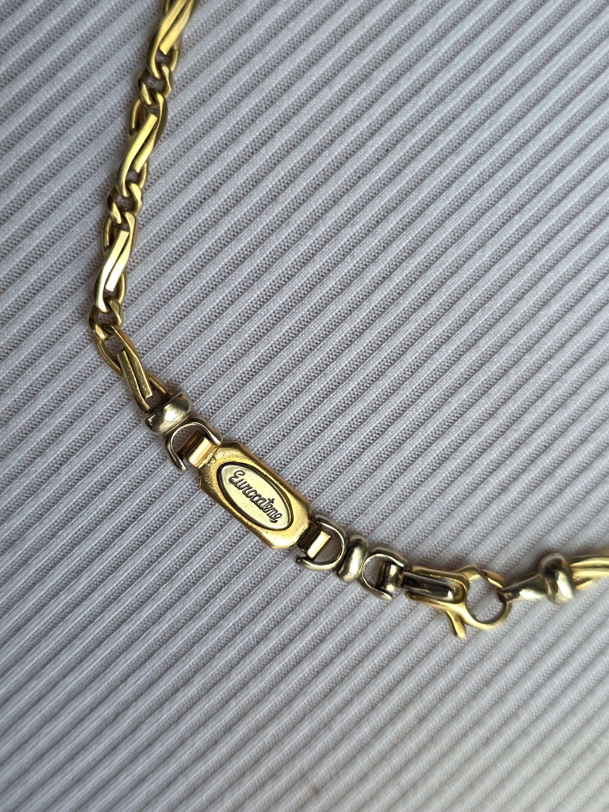 Gold chain bracelet with a visible brand logo on a gray textured background