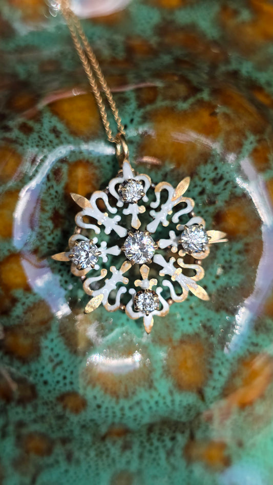 A close-up of a snowflake-shaped pendant necklace with clear gemstones and gold-toned filigree details, hanging against a glossy green and brown marbled surface.