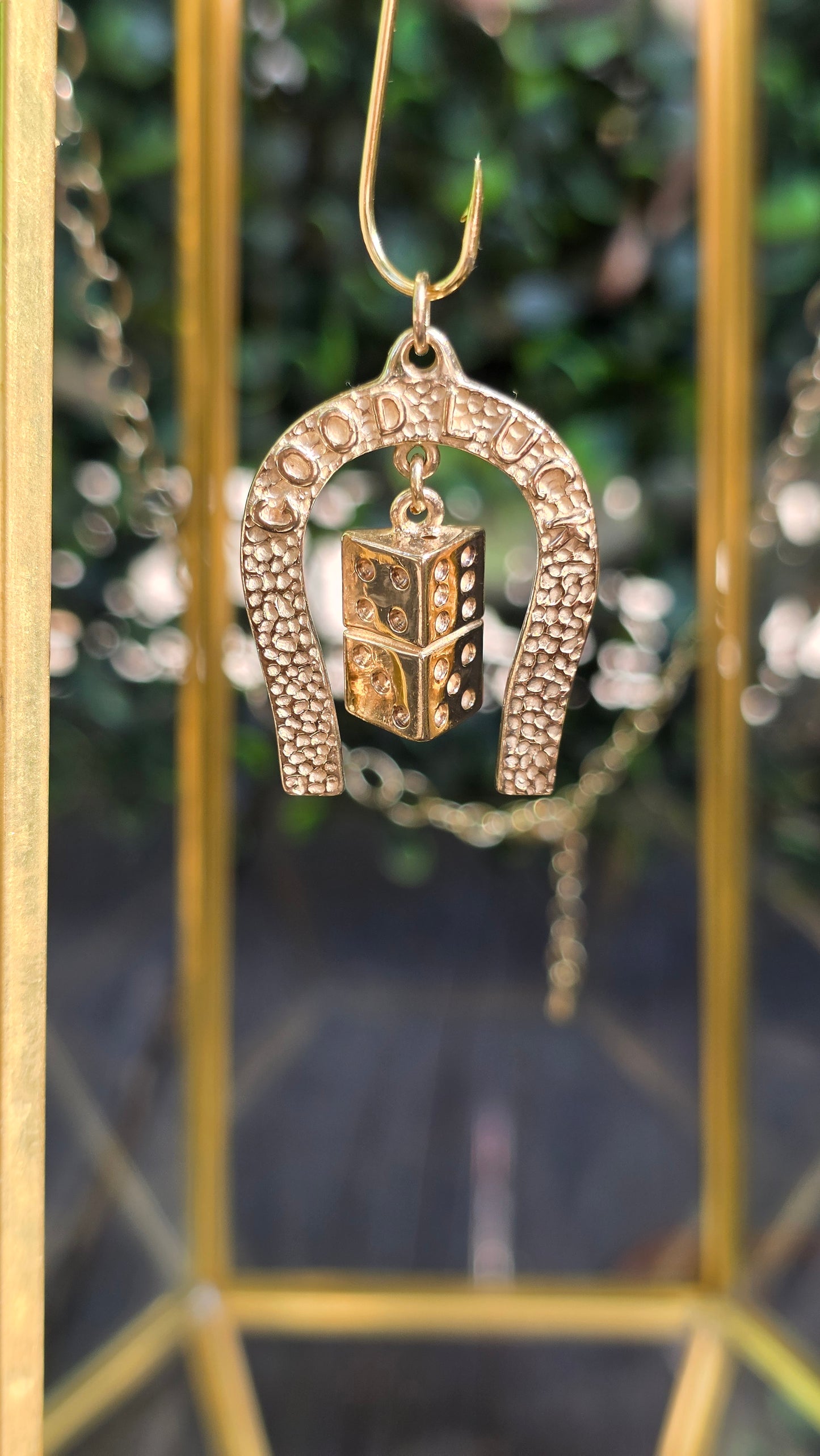 A gold-toned horseshoe earring featuring a small, detailed miniature chest charm, displayed against a blurred background with gold geometric frames.