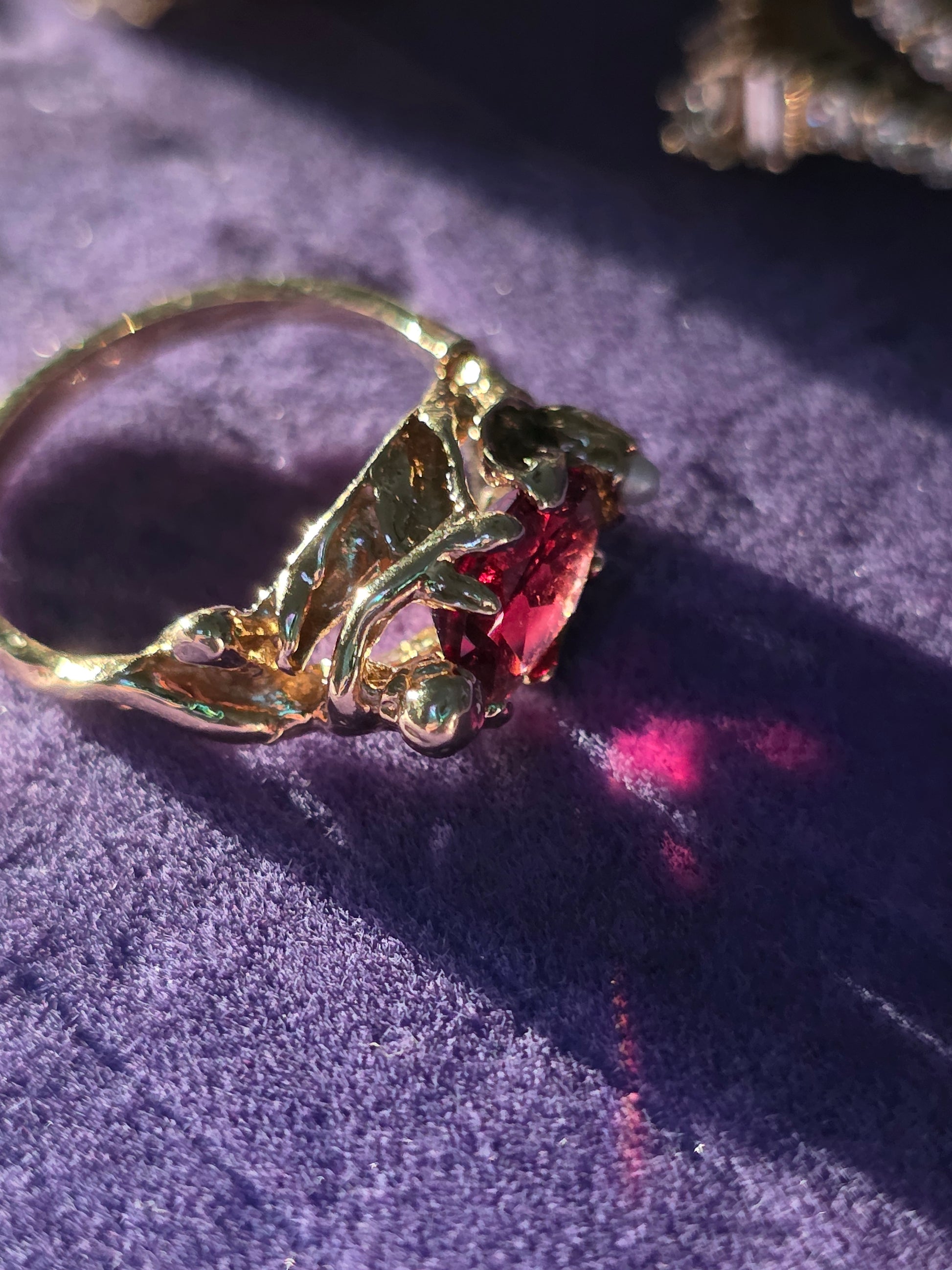 Gold ring with a red gemstone on a textured purple surface