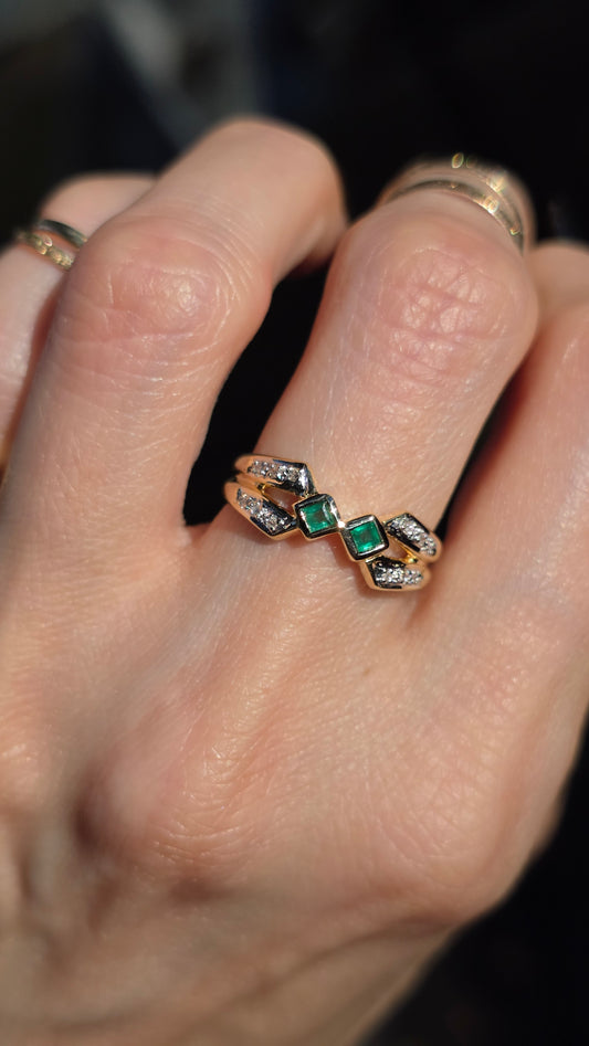 A close-up of a hand wearing a gold ring with three green square-cut stones and small clear stones, alongside other rings on adjacent fingers.
