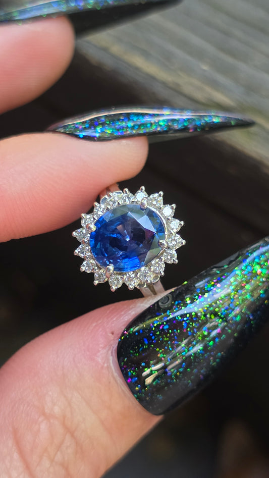 Close-up of a blue gemstone ring held between fingers with colorful nail polish.