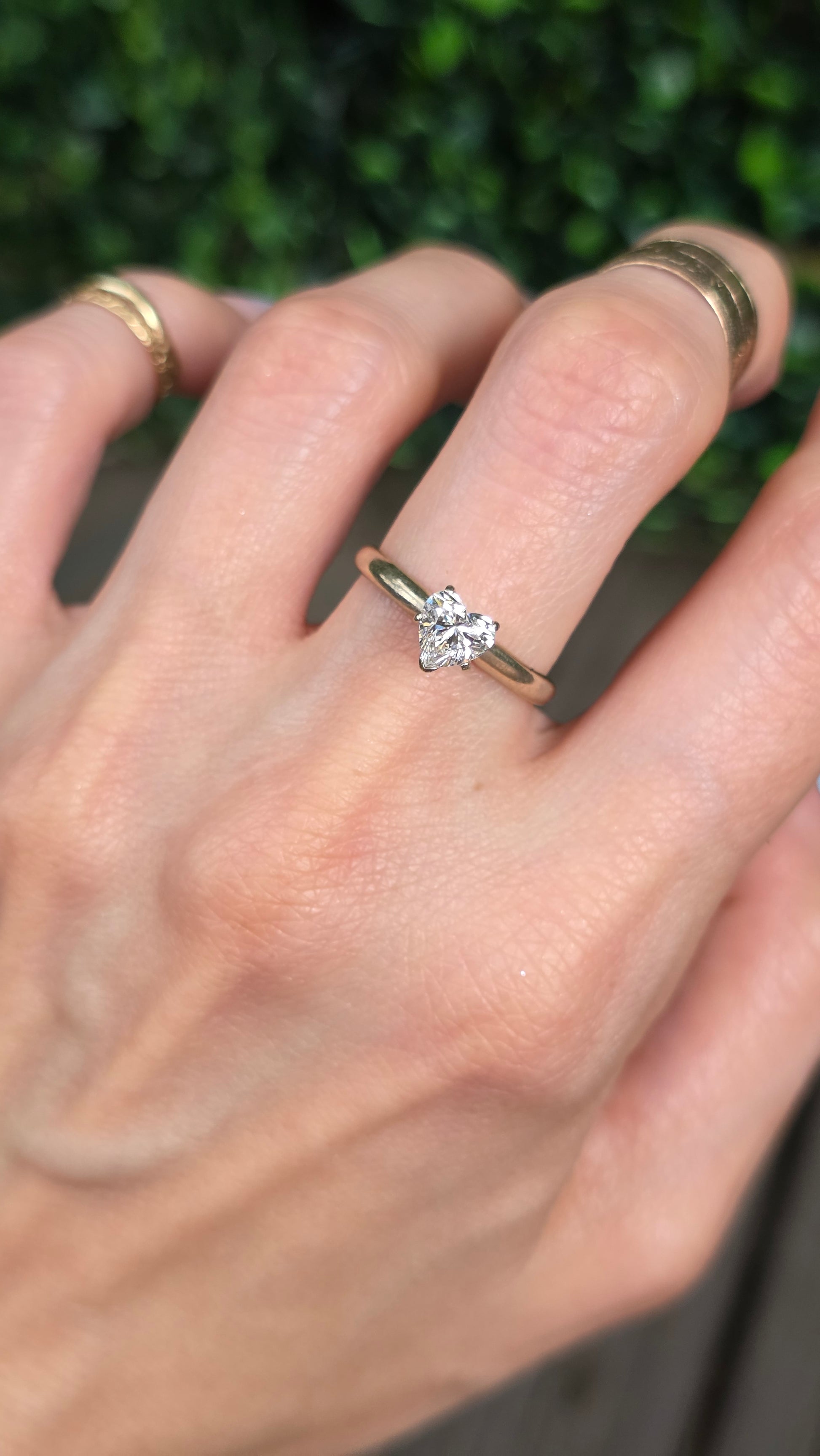 A close-up of a hand wearing a silver four-petal flower ring with a clear center gemstone, alongside other gold rings on other fingers.