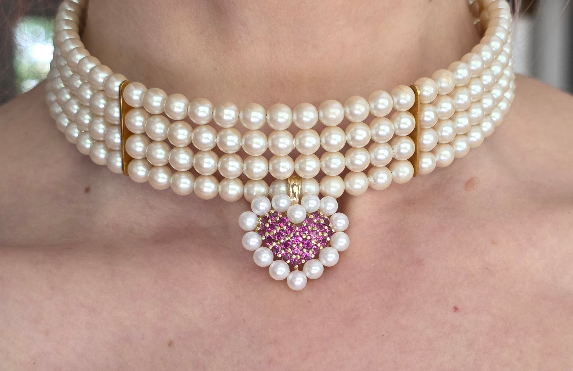 Pearl necklace with a heart-shaped gemstone pendant on a person's neck.