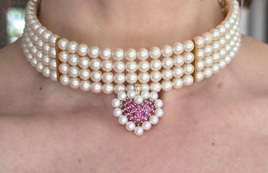 Pearl necklace with a heart-shaped gemstone pendant on a person's neck.