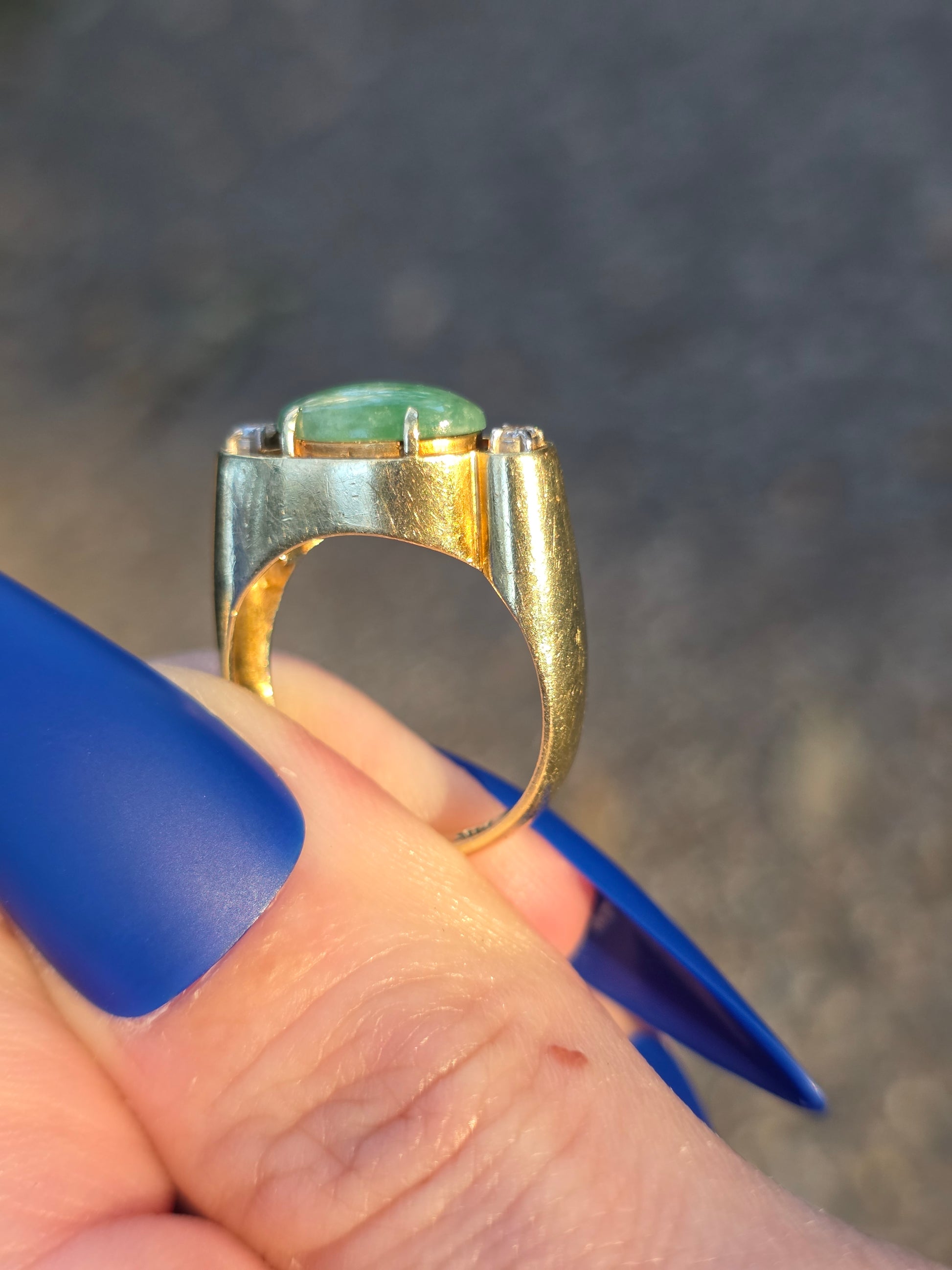 Gold ring with a green gemstone held by a hand with blue nail polish.