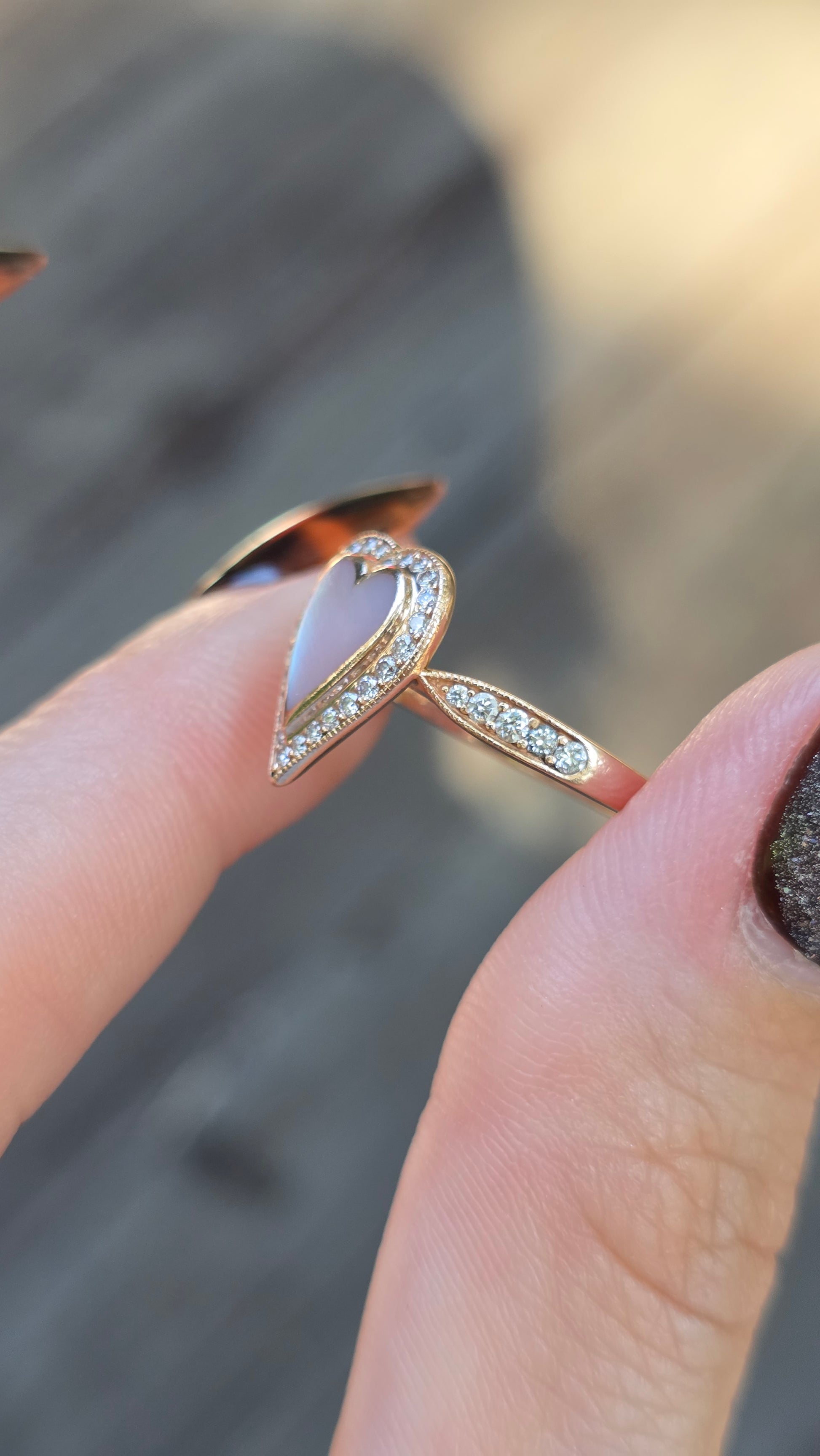 Gold ring with a pink stone held between fingers against a blurred background