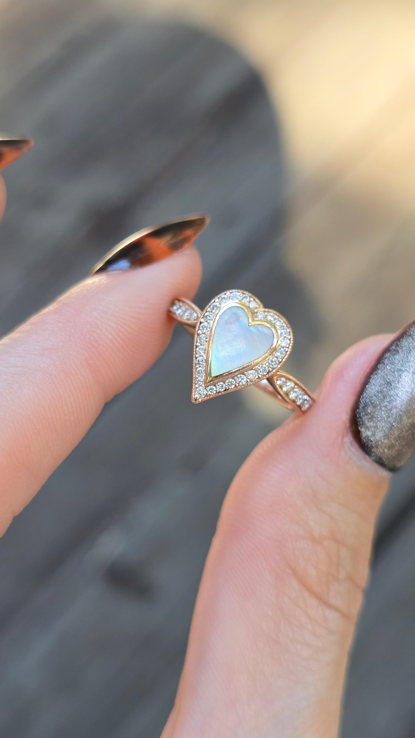 Heart-shaped opal ring with diamond accents held between fingers against a blurred background