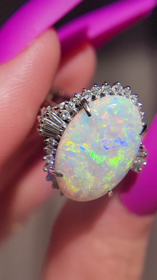 This beautiful ballerina style Opal ring is crafted in gorgeous platinum and weighs in at approximately 9.8 grams. She features an incredibly vivid center Opal that is approximately 5.6ct. The center stone is guarded by a sparkly tutu with approximately .57ct of stunning diamonds. This ring will certainly make you feel like belle of the ball. Don't miss your opportunity to dance with this sparkler. 