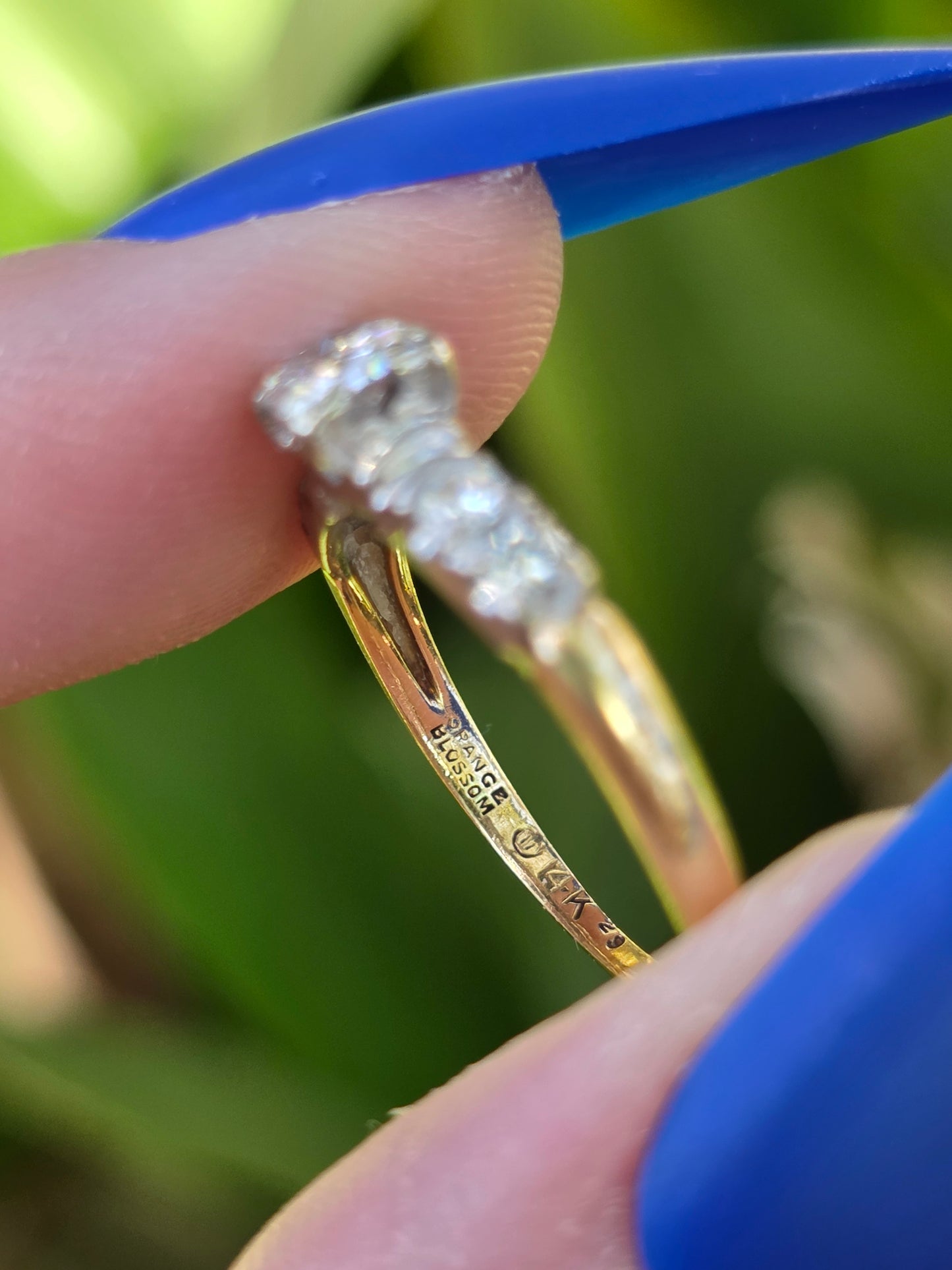 Gold ring with diamonds held between fingers against a blurred green background