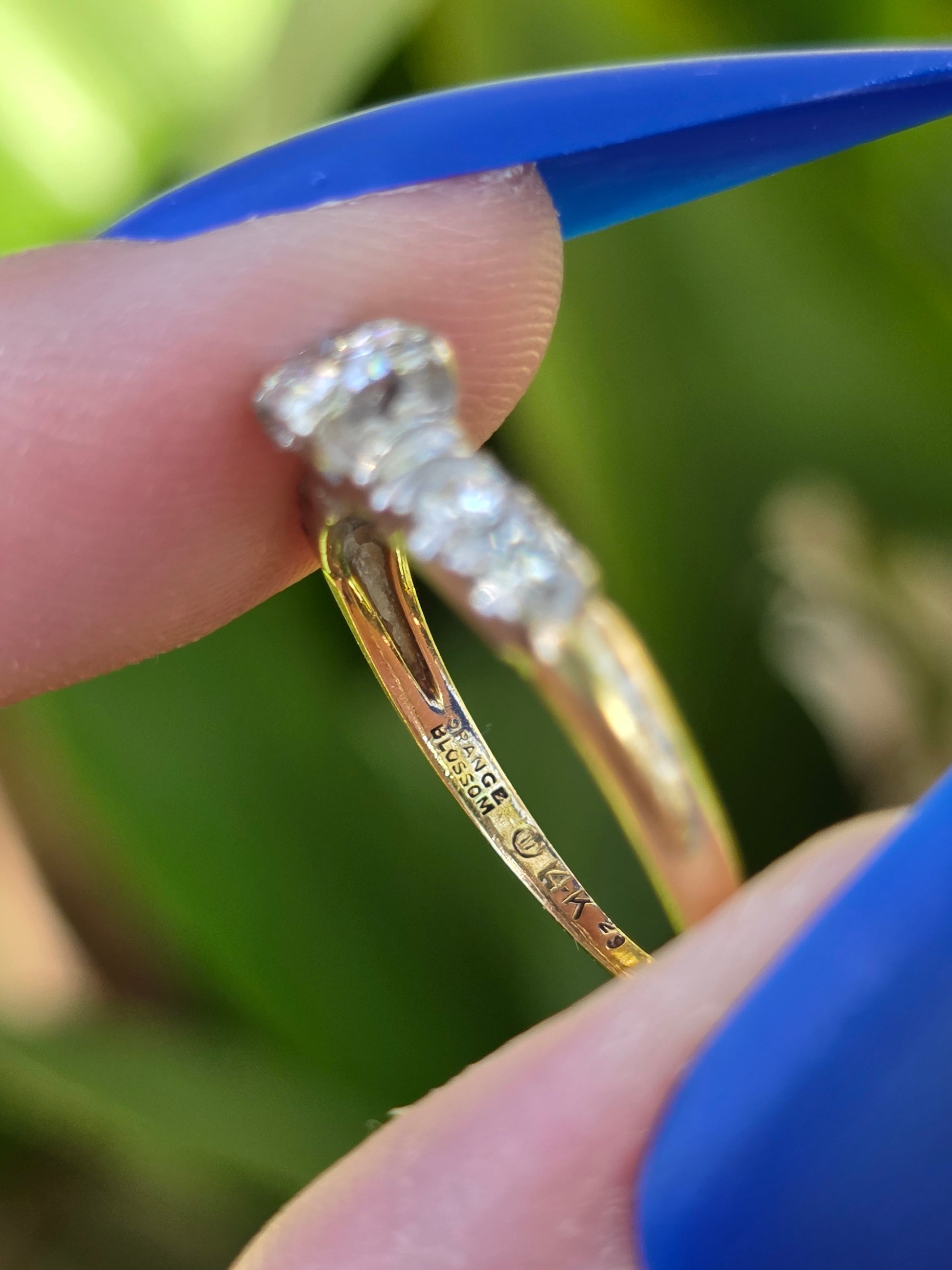 Gold ring with diamonds held between fingers against a blurred green background