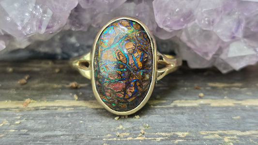 Ring with an intricate design on a wooden surface with purple crystals in the background