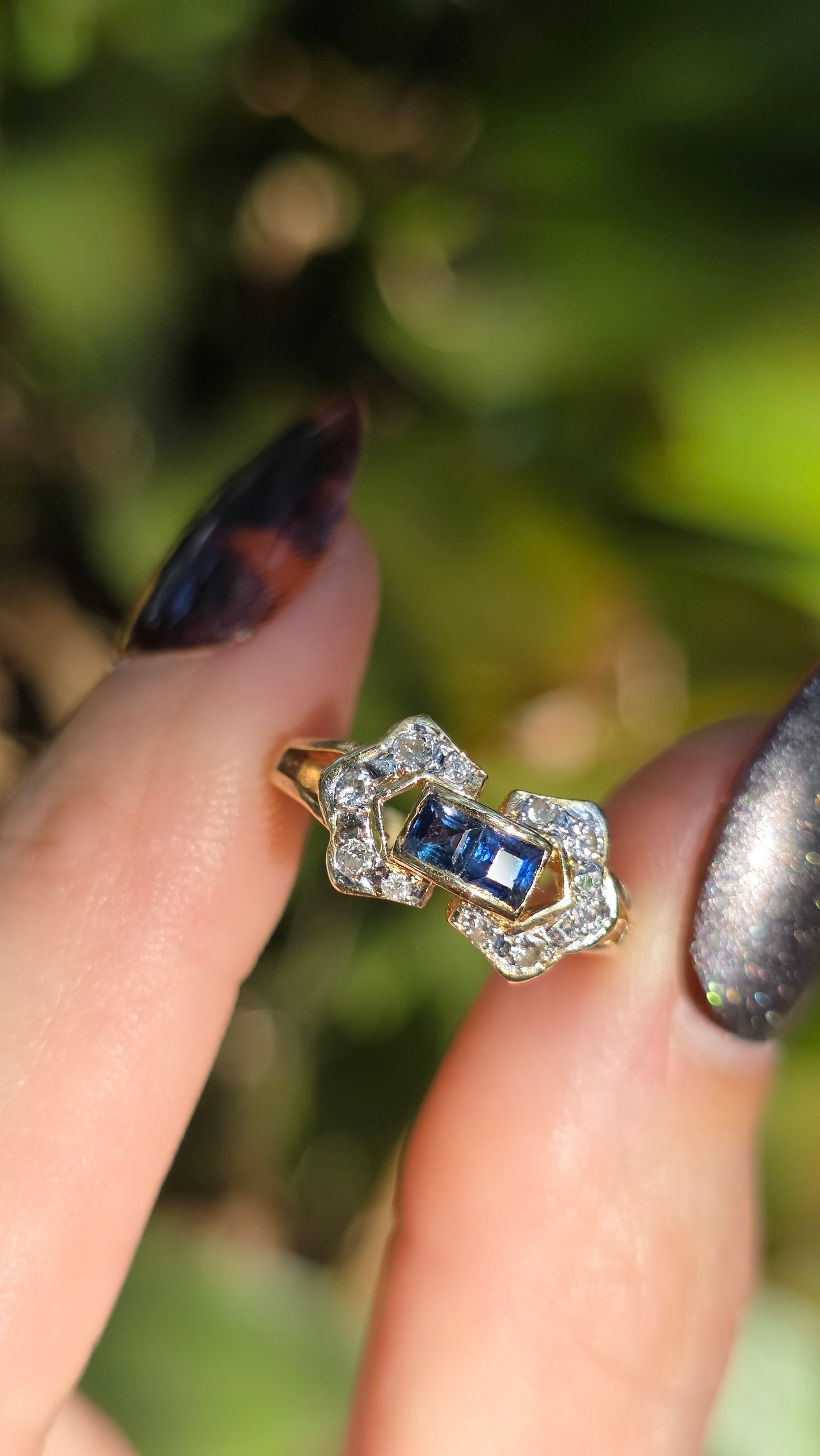 Gold ring with a blue gemstone on a finger against a blurred green background