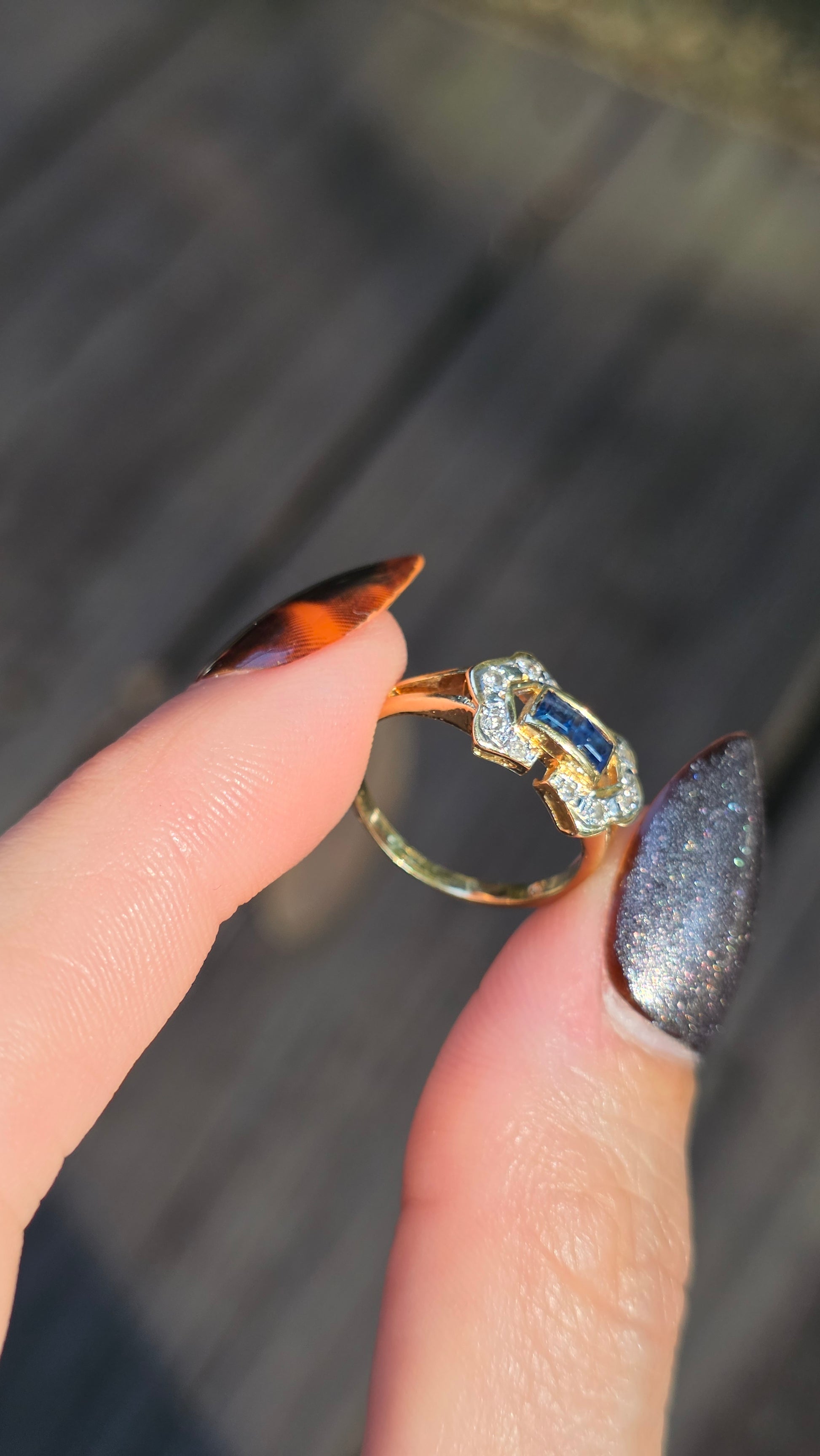 Gold ring with a blue gemstone held between fingers against a blurred background