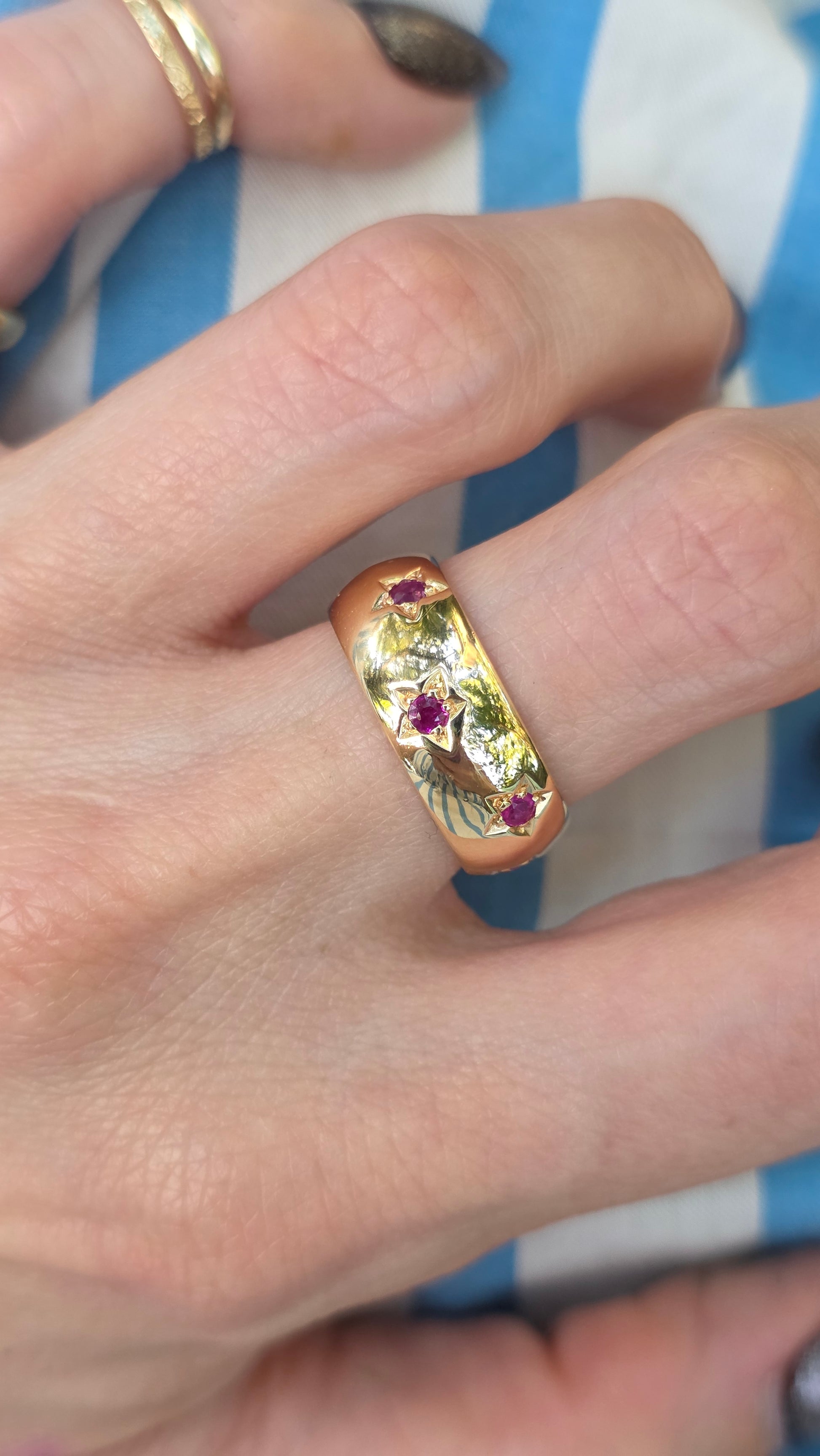Gold ring with gemstones on a person's finger against a striped fabric background