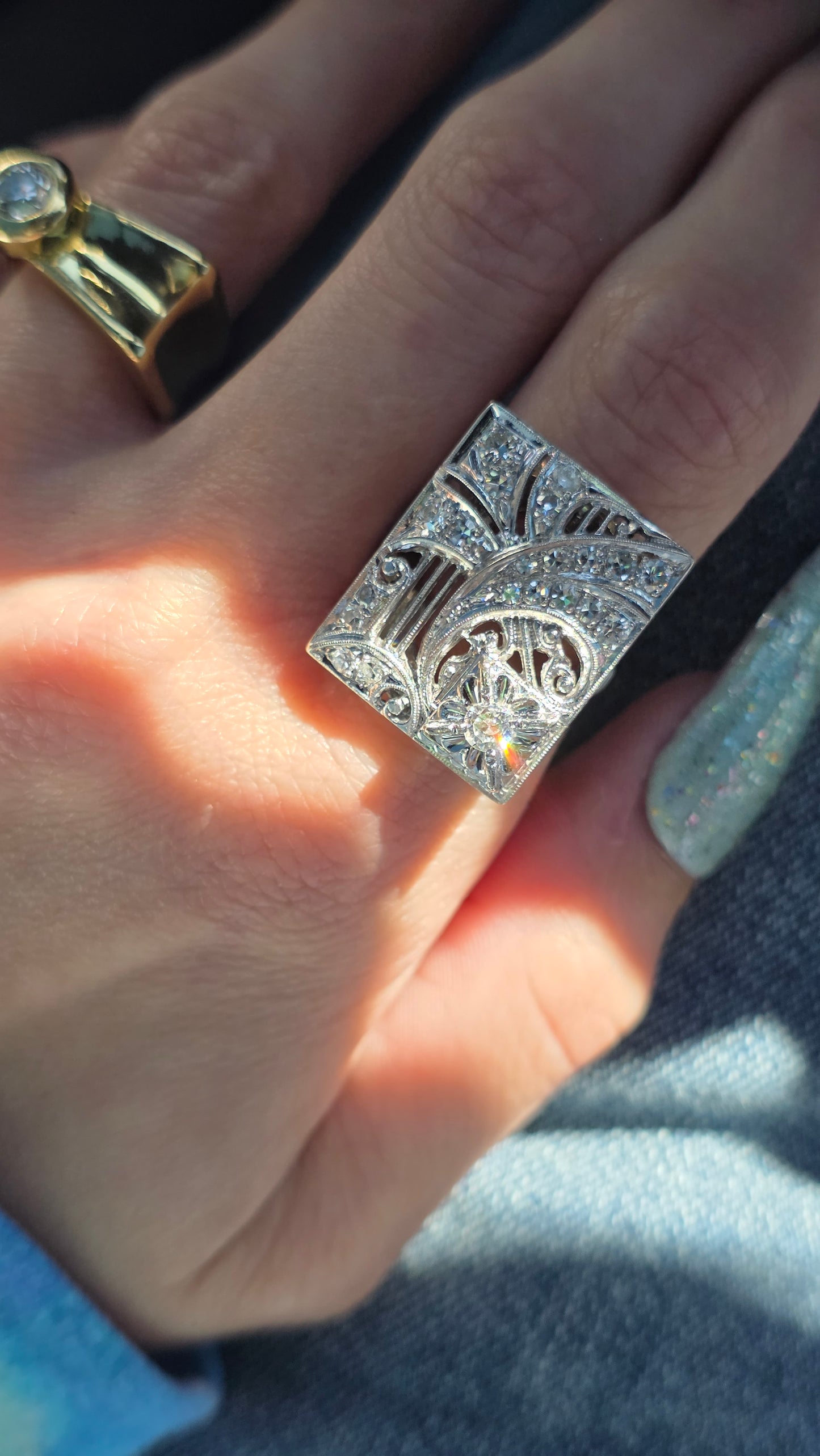 Close-up of a hand wearing a white gold ring with intricate design.