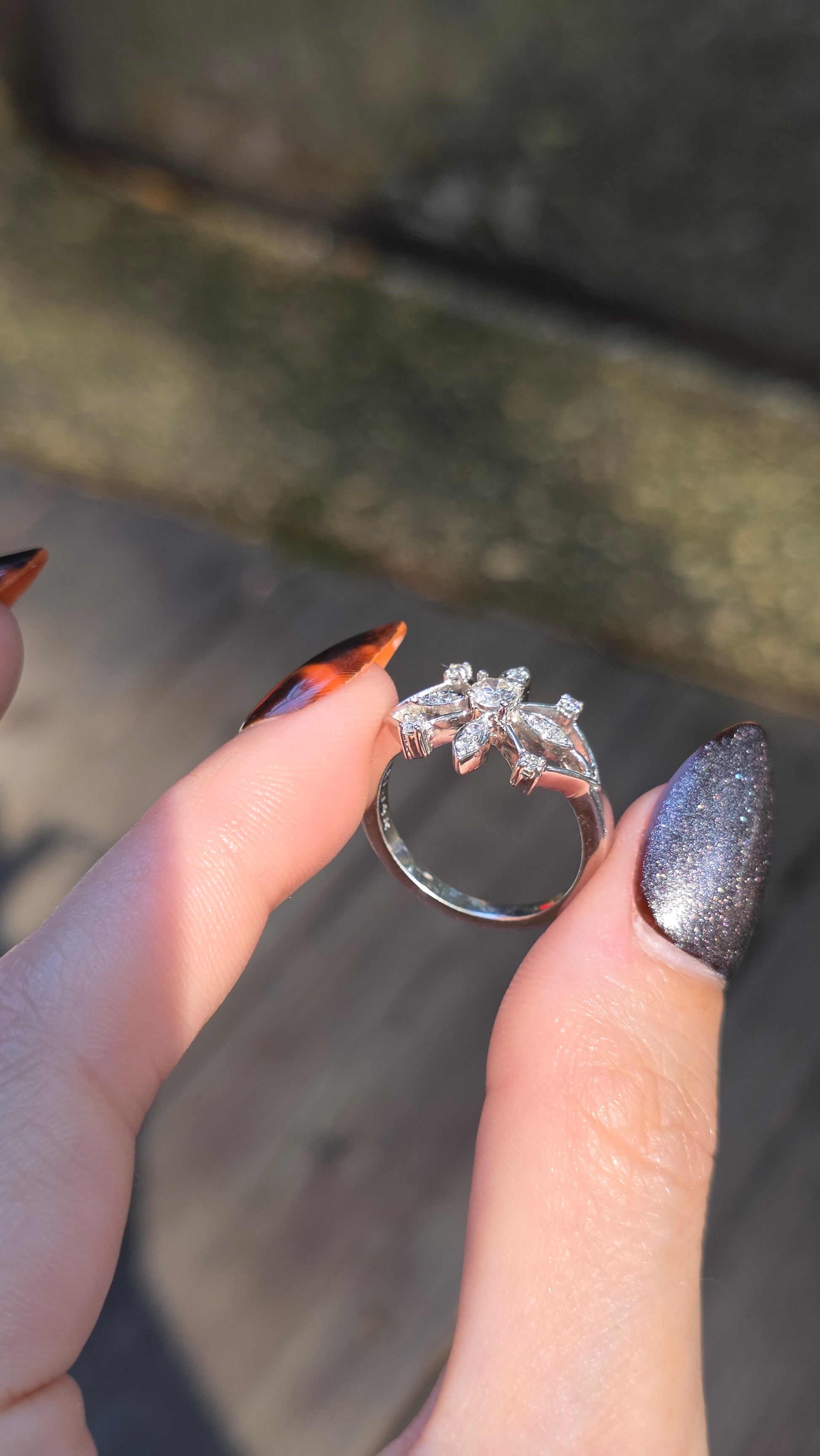 Silver ring with a diamond held between fingers against a blurred natural background