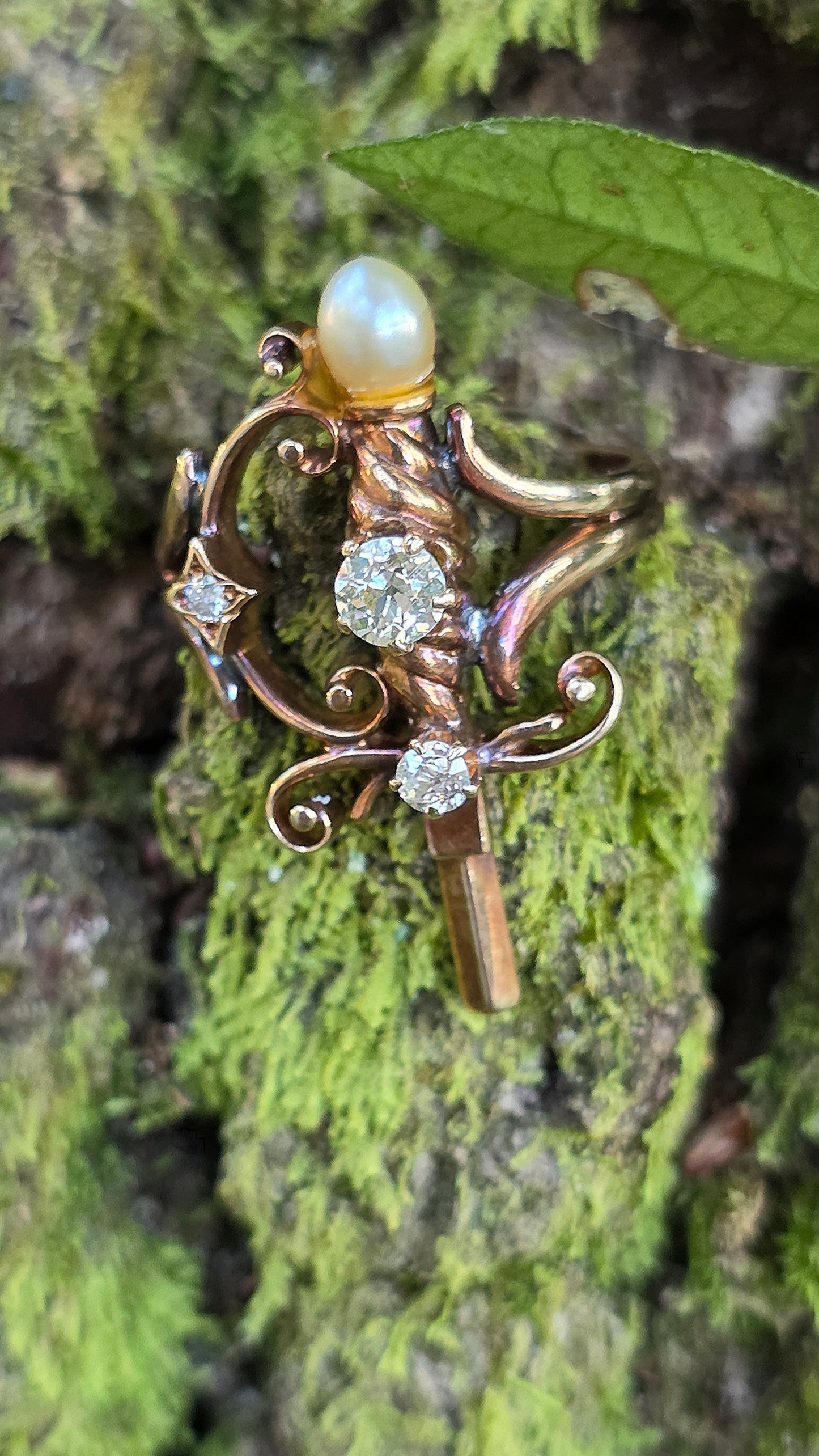 Vintage-style ring with pearl and gemstones on a textured green surface