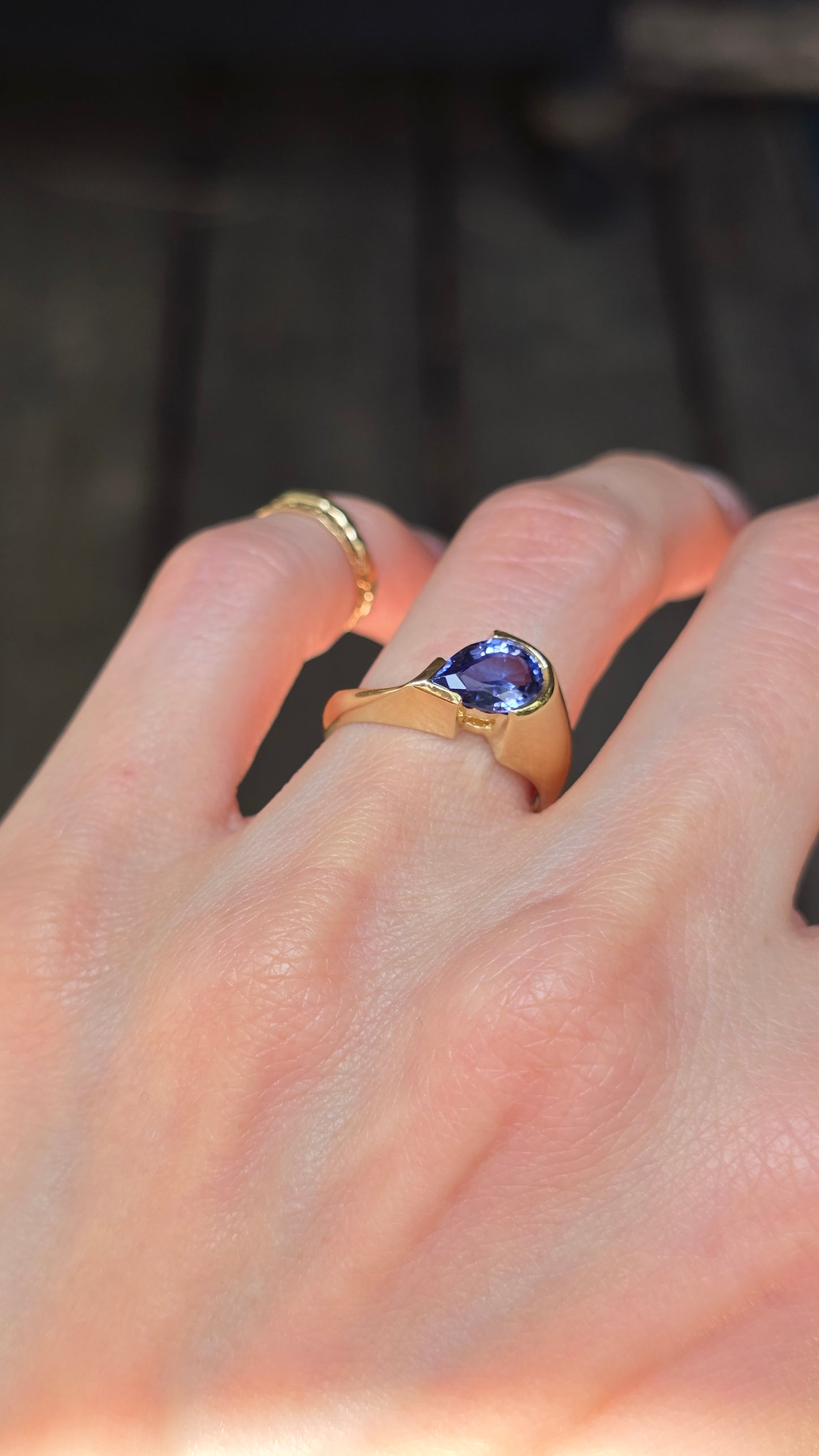 Gold ring with a purple gemstone on a hand against a blurred background