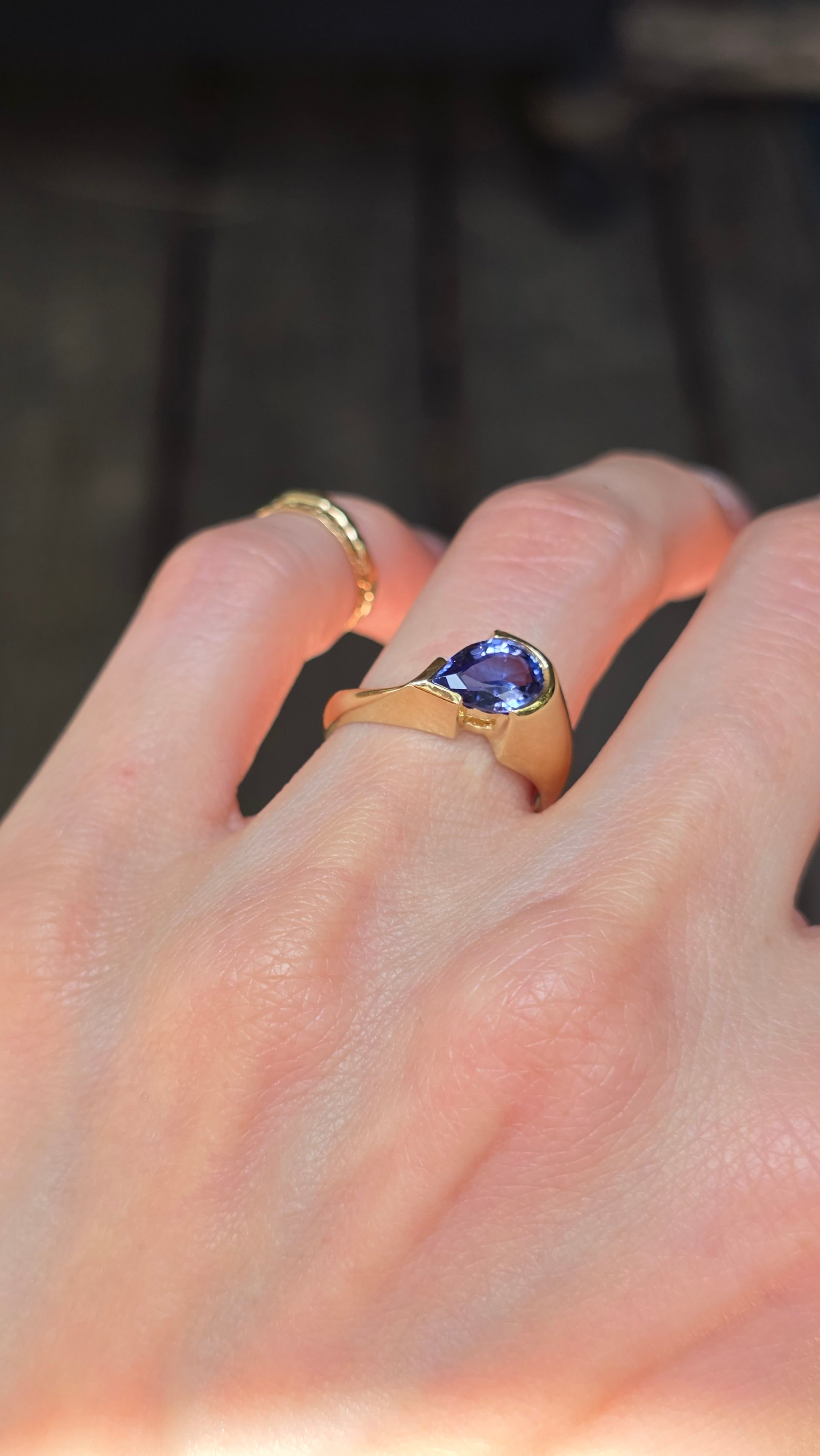 Gold ring with a purple gemstone on a hand against a blurred background