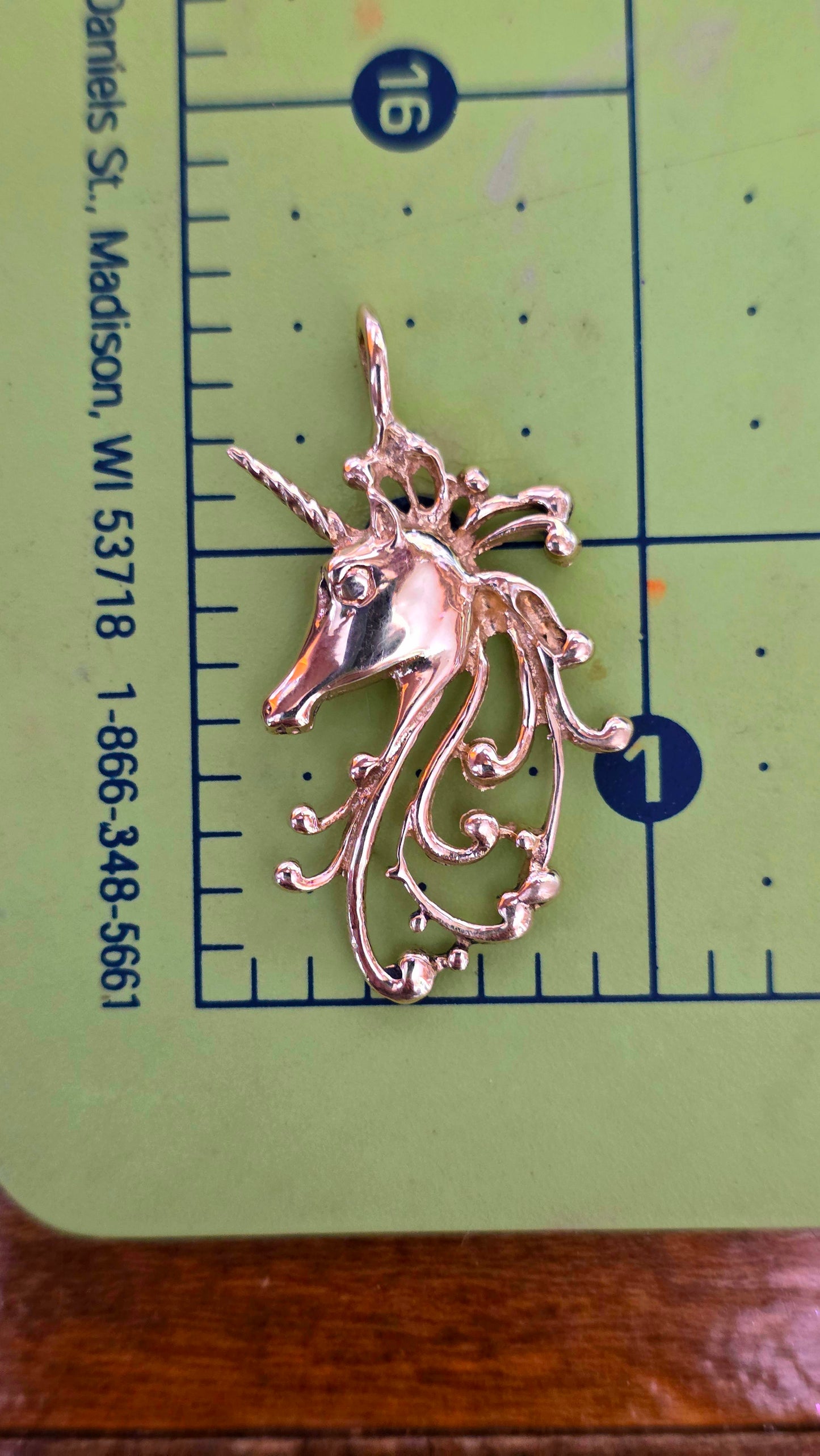 Gold unicorn pendant on a green cutting mat with ruler for scale.