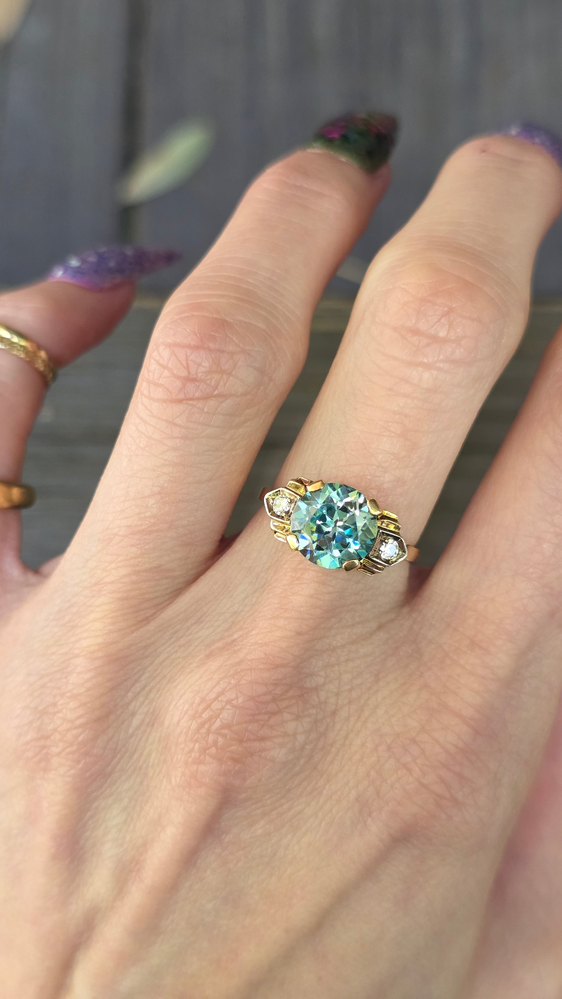 Close-up of a hand wearing a gold ring with a blue gemstone.